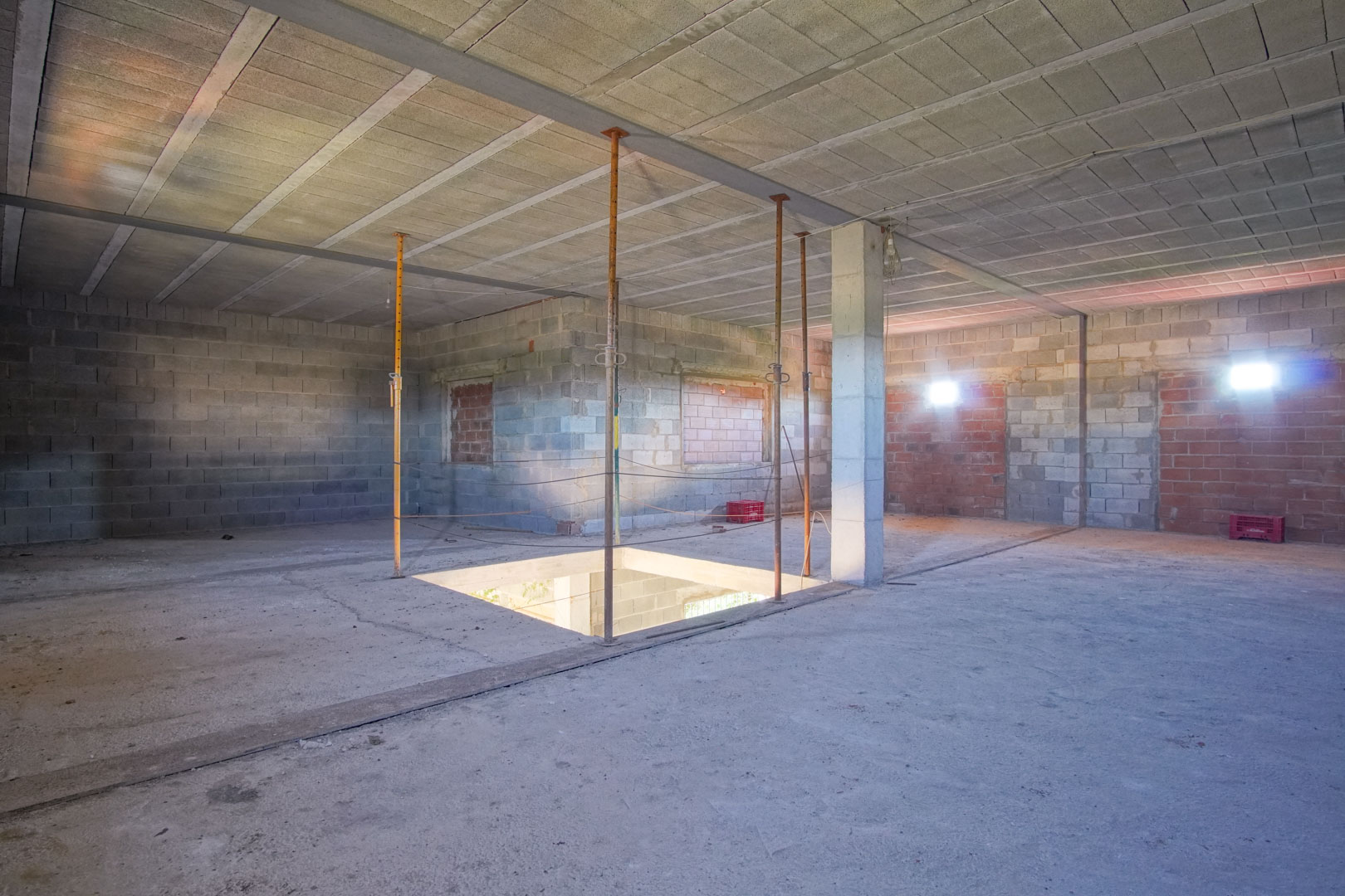Planta superior diáfana en estado de obra, con estructura de hormigón vista, pilares de soporte y hueco central para futura escalera.