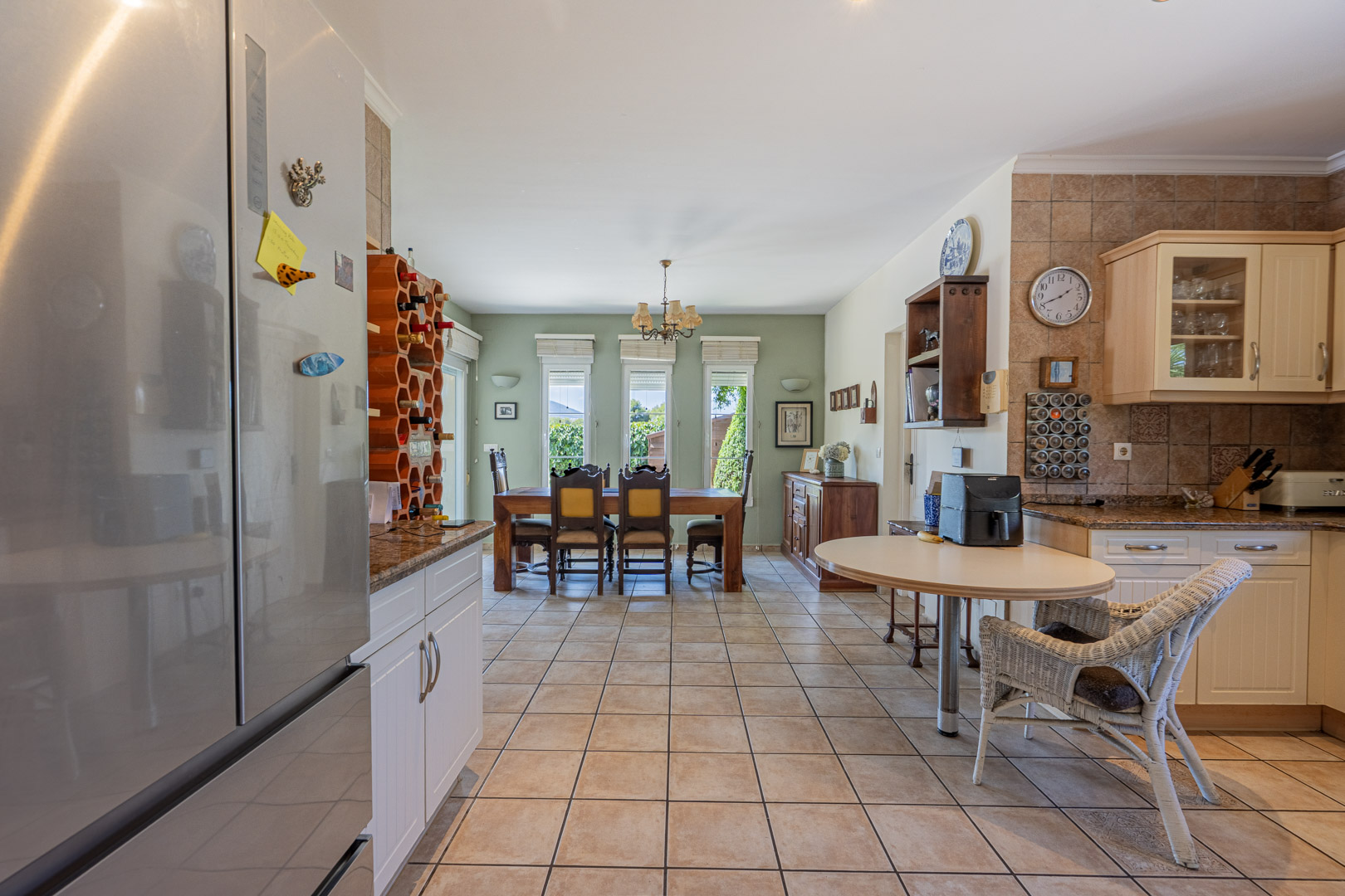 Cocina espaciosa con mesa de comedor de madera, armarios blancos y estante para vinos tipo panal.