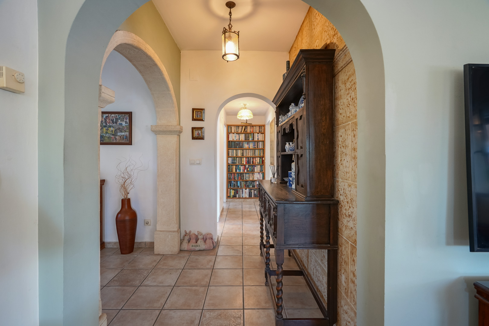 Pasillo con arcos de piedra y librería al fondo. Mueble de madera oscura.