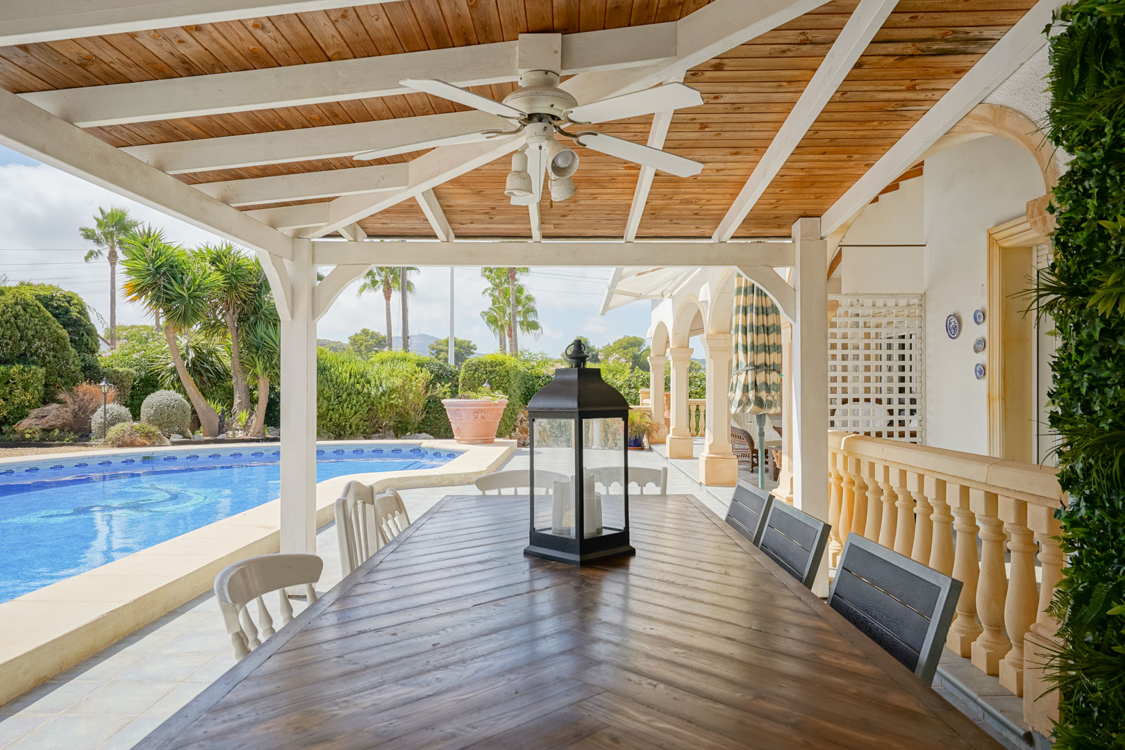 Terraza cubierta con mesa de madera, vistas a la piscina y jardín en Jávea.