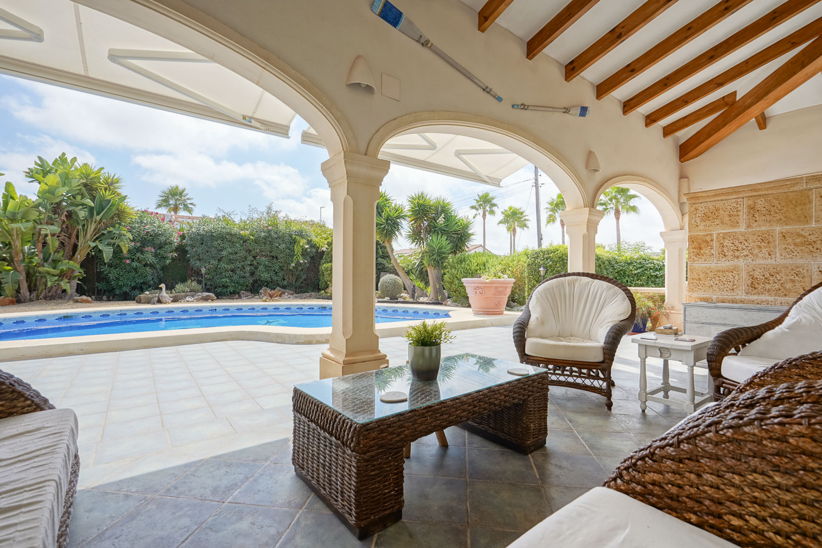 Terraza cubierta con vistas a la piscina. Mobiliario de ratán y mesa de centro de cristal.