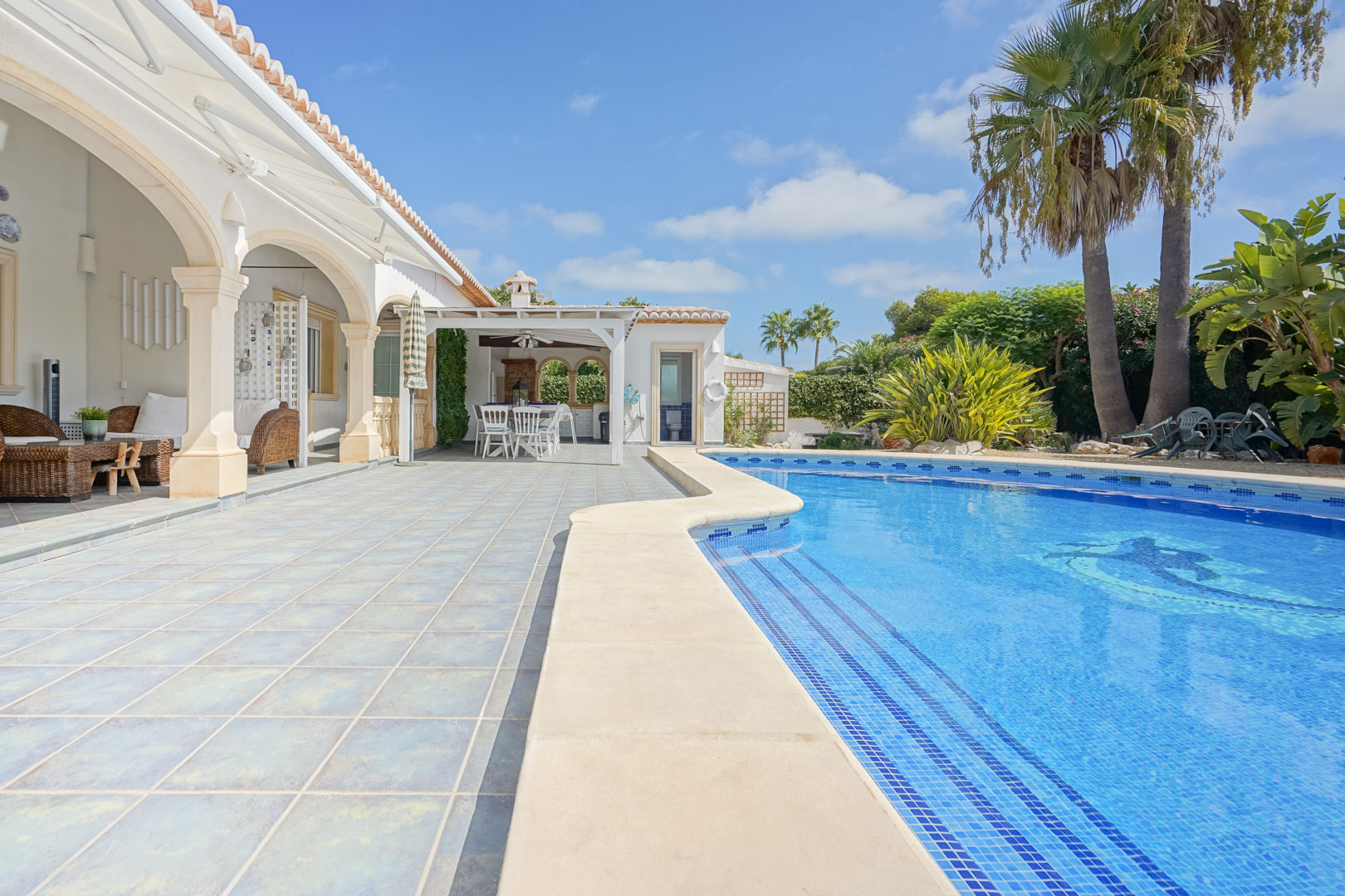 Vista de la piscina con mosaicos azules y terraza con columnas de piedra en Jávea.
