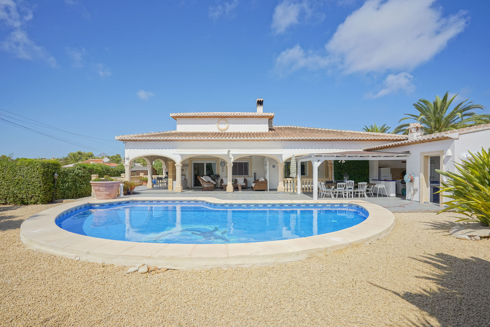 Vista de la piscina con mosaicos y la terraza cubierta con arcos de una villa en Jávea.