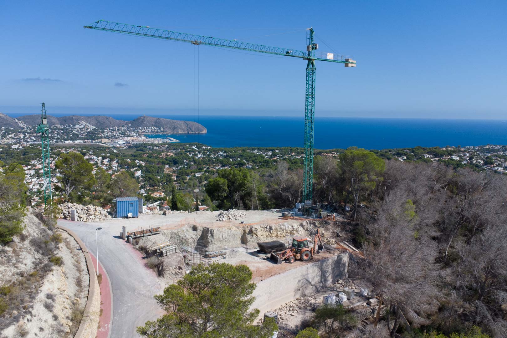 Vista aérea de la parcela en fase inicial de construcción, con grúa torre y excavación sobre una colina con vistas panorámicas al mar Mediterráneo en Moraira.