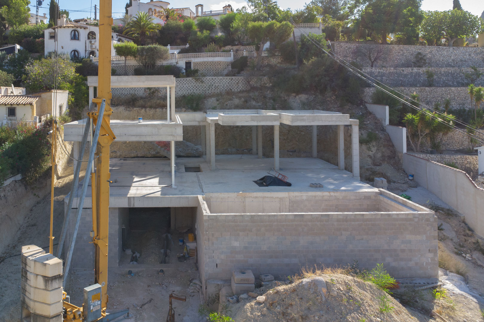 Vista de la estructura de hormigón armado en fase de construcción, mostrando los diferentes niveles de la villa y el entorno de muros de piedra natural.