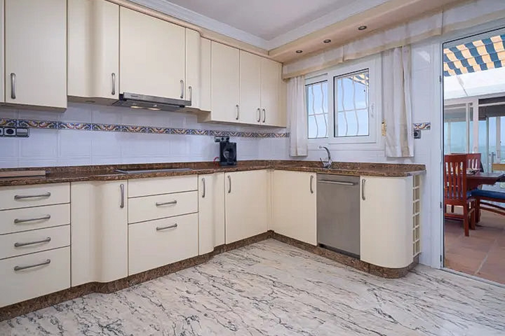 Cocina equipada con mobiliario en tono crema, encimeras de granito y suelos de mármol. Dispone de acceso directo a la terraza y abundante luz natural.