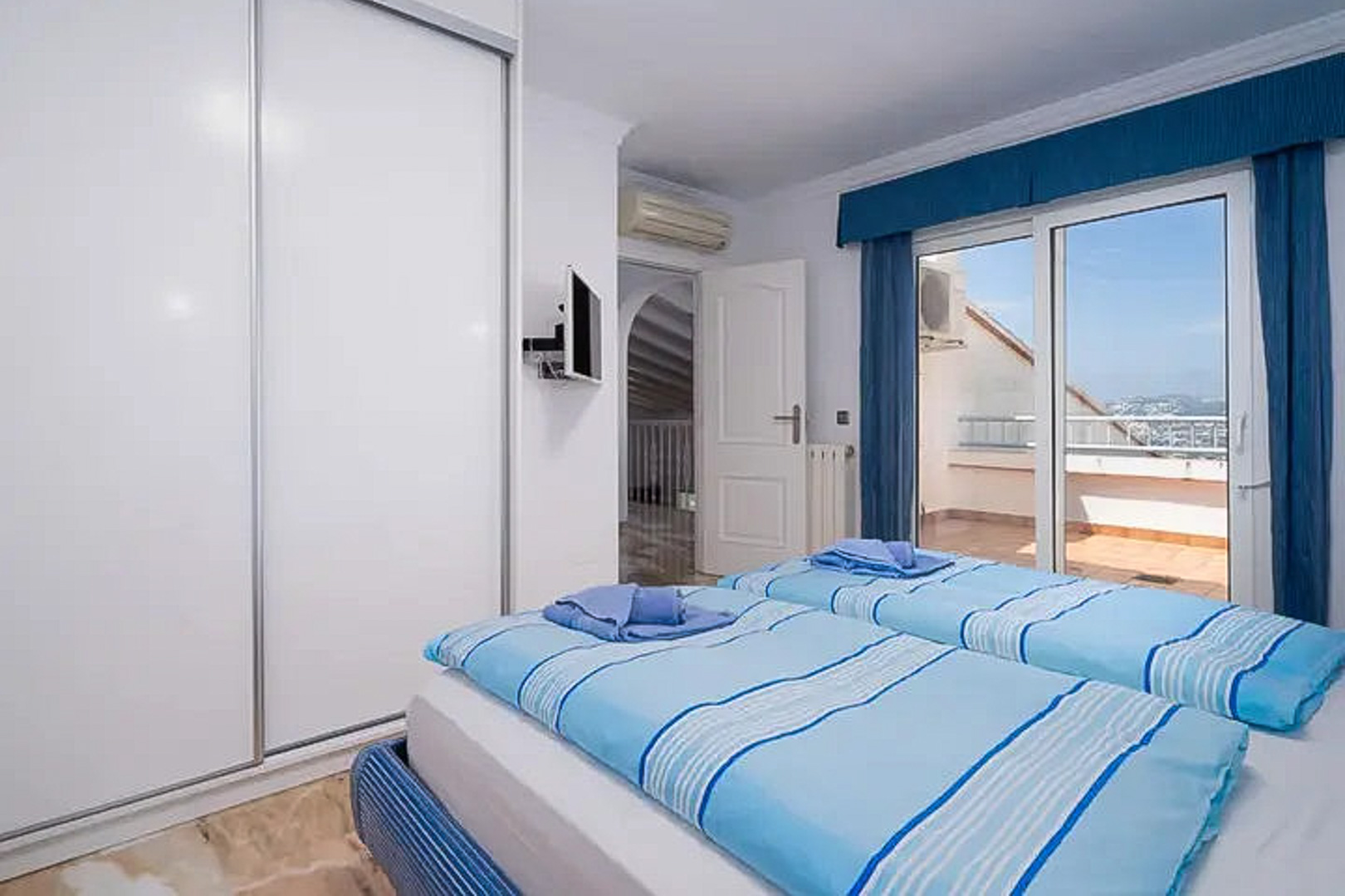 Dormitorio con dos camas individuales, amplio armario de puertas correderas blancas y acceso directo a una terraza privada con vistas. Incluye aire acondicionado y TV de pared.