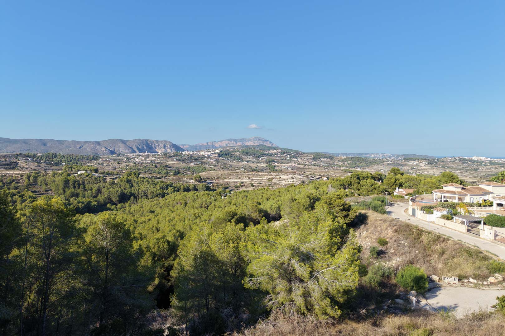 Vistas panorámicas despejadas hacia el valle y las montañas, rodeadas de densos pinares mediterráneos bajo un cielo despejado en Moraira.