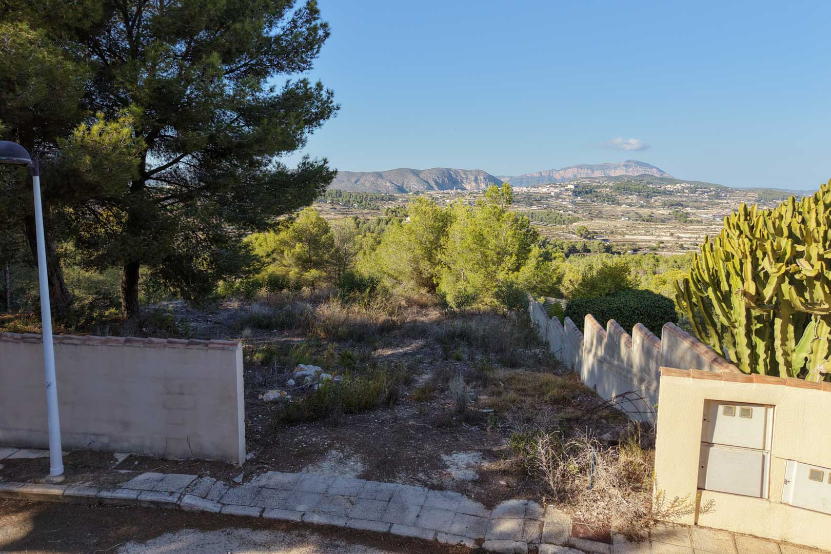 Parcela urbana elevada en Benimeit con vistas despejadas al valle y montañas. Incluye acceso asfaltado, muros perimetrales y vegetación autóctona bajo un cielo despejado.