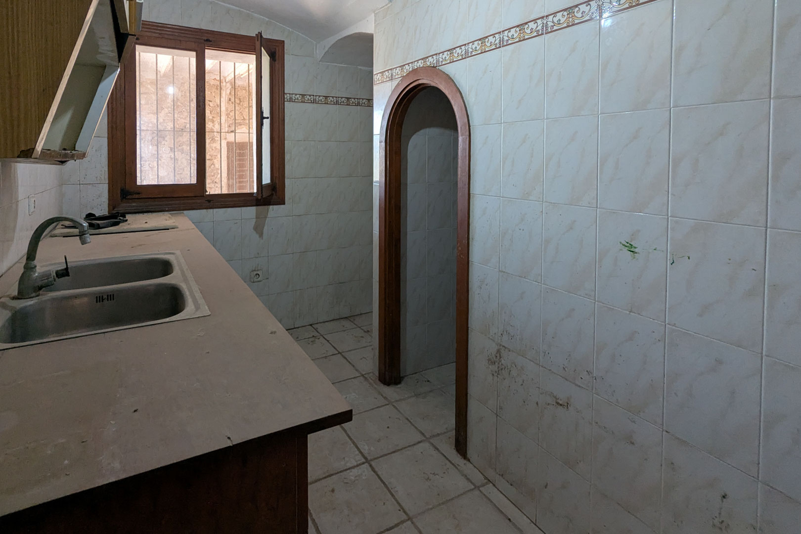Cocina rústica original con fregadero doble de acero inoxidable, paredes alicatadas con cenefa decorativa y un arco de madera que da paso a otras estancias.