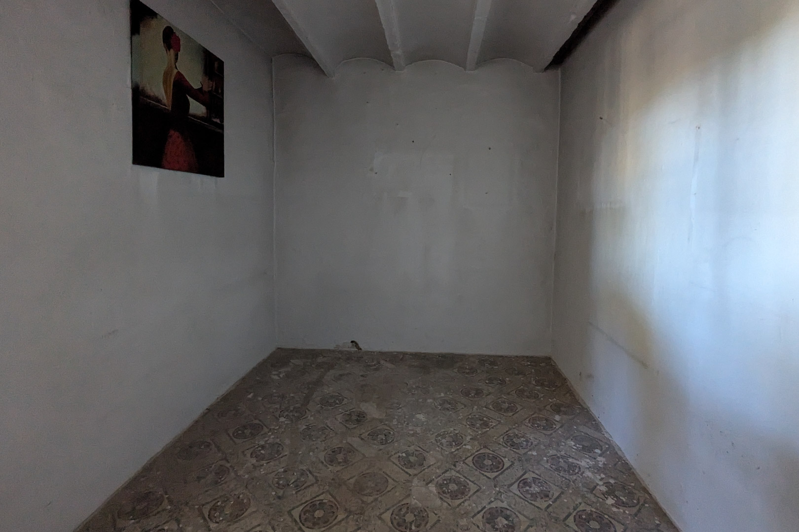 Habitación interior con suelo hidráulico tradicional y techo de vigas revestidas. Las paredes blancas y la luz natural resaltan la esencia rústica de esta estancia a reformar.