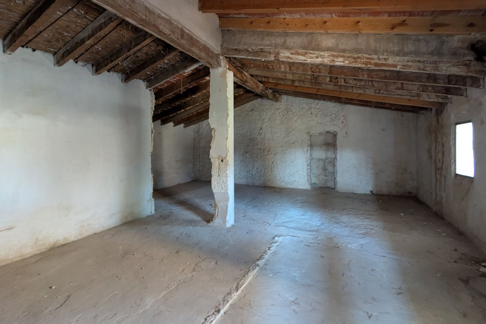 Planta superior diáfana que muestra la estructura original de vigas de madera de almendro, techos de caña y paredes de cal con una ventana lateral.