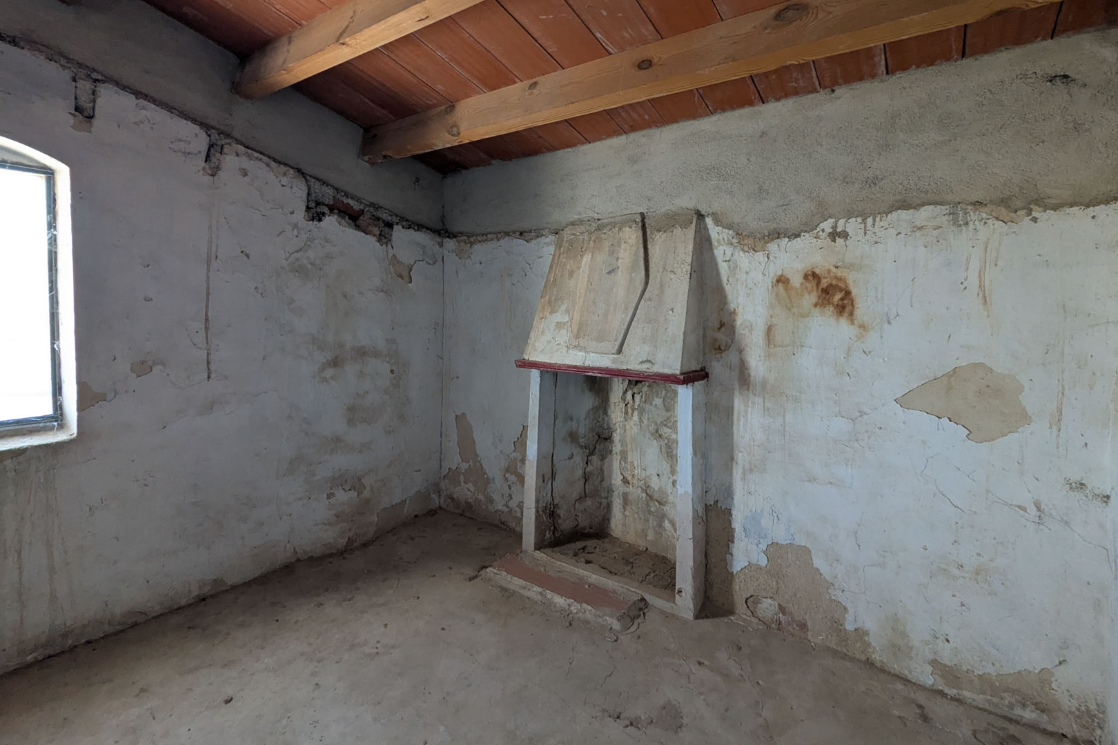 Salón rústico con chimenea tradicional de campana, vigas de madera vista en el techo y paredes de cal que muestran la estructura original de piedra.