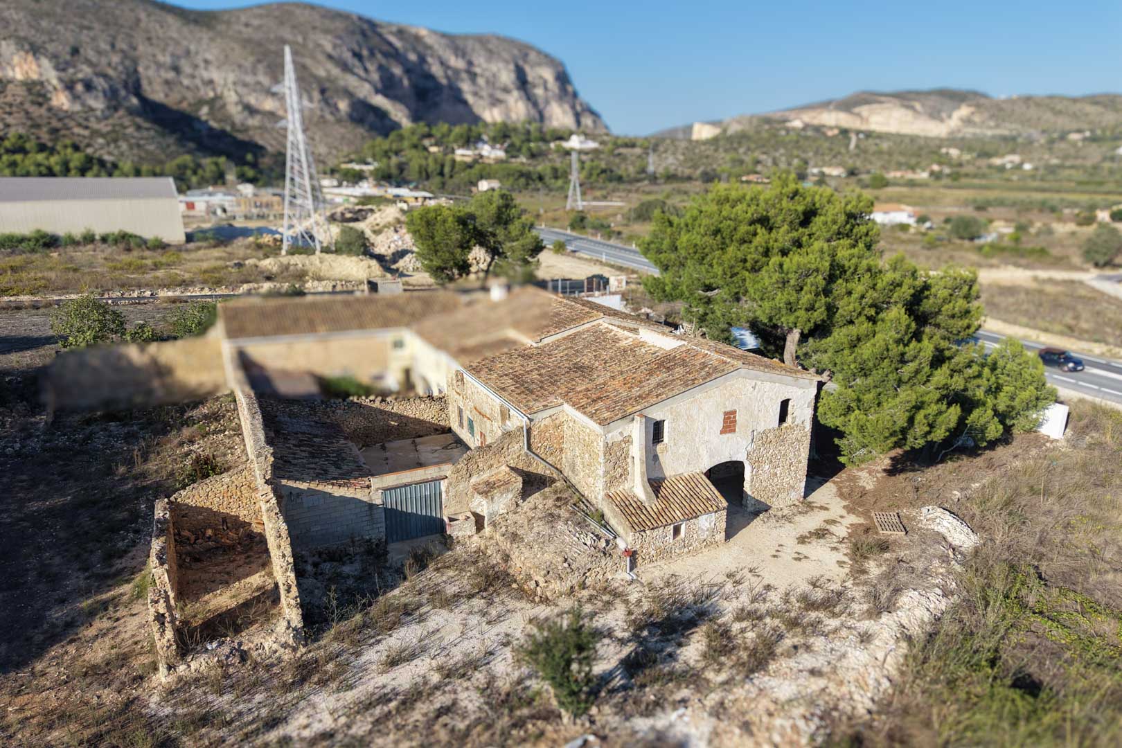 Vista aérea de la casa de campo tradicional con muros de piedra natural, cubiertas de teja cerámica y estructuras anexas en un entorno rural.