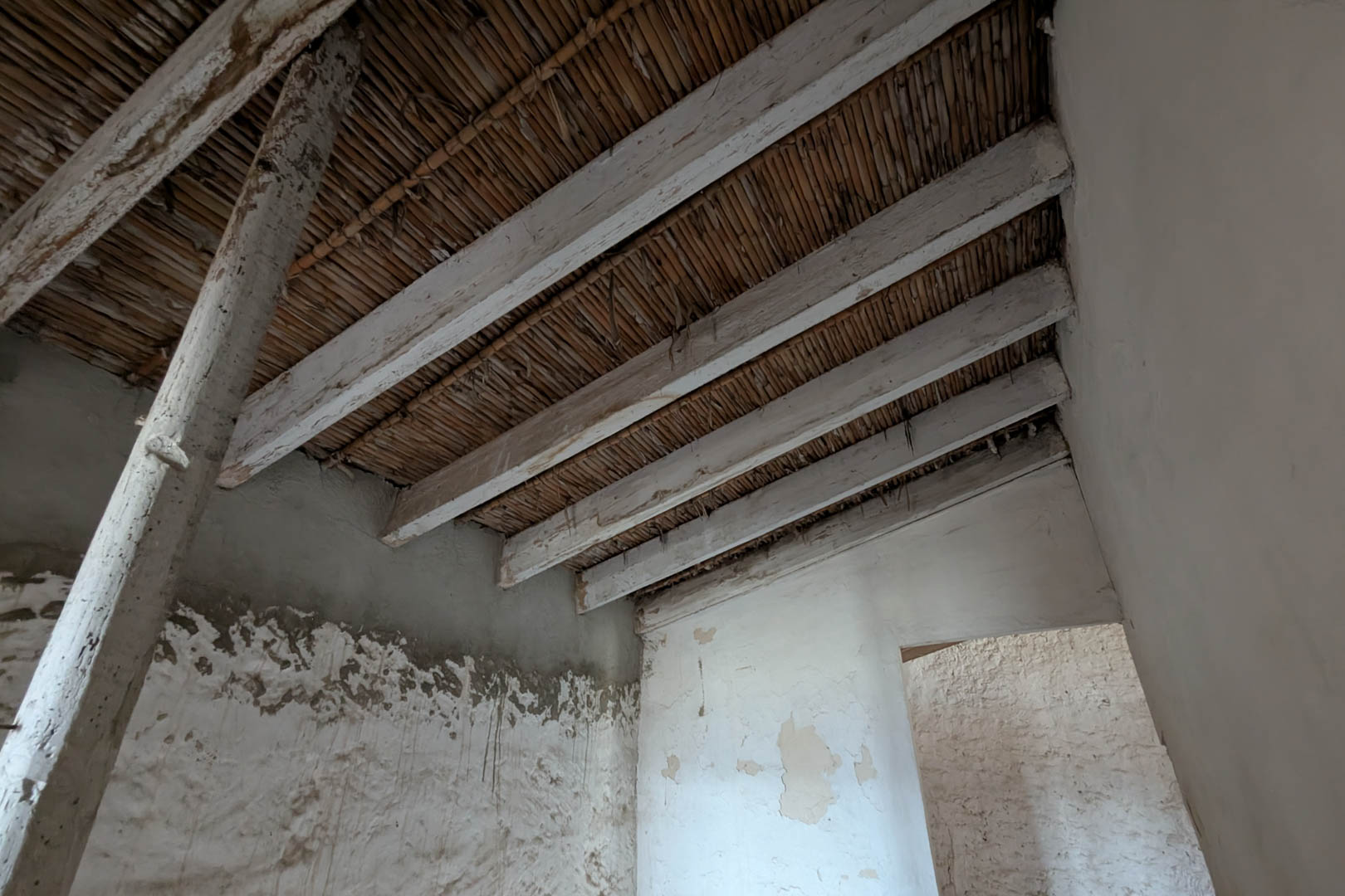 Vista interior que muestra el techo original de cañizo y vigas de madera encaladas. Las paredes de piedra natural conservan el revestimiento de cal tradicional.