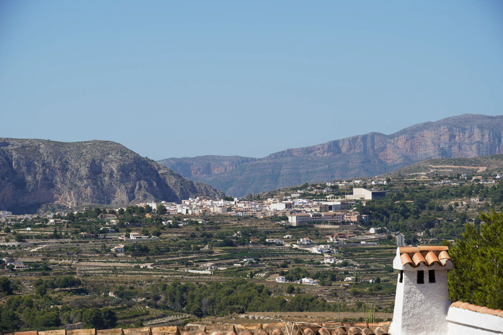 Vistas panorámicas desde la propiedad hacia el pueblo de Teulada, mostrando el paisaje de bancales agrícolas y las montañas circundantes bajo un cielo despejado.