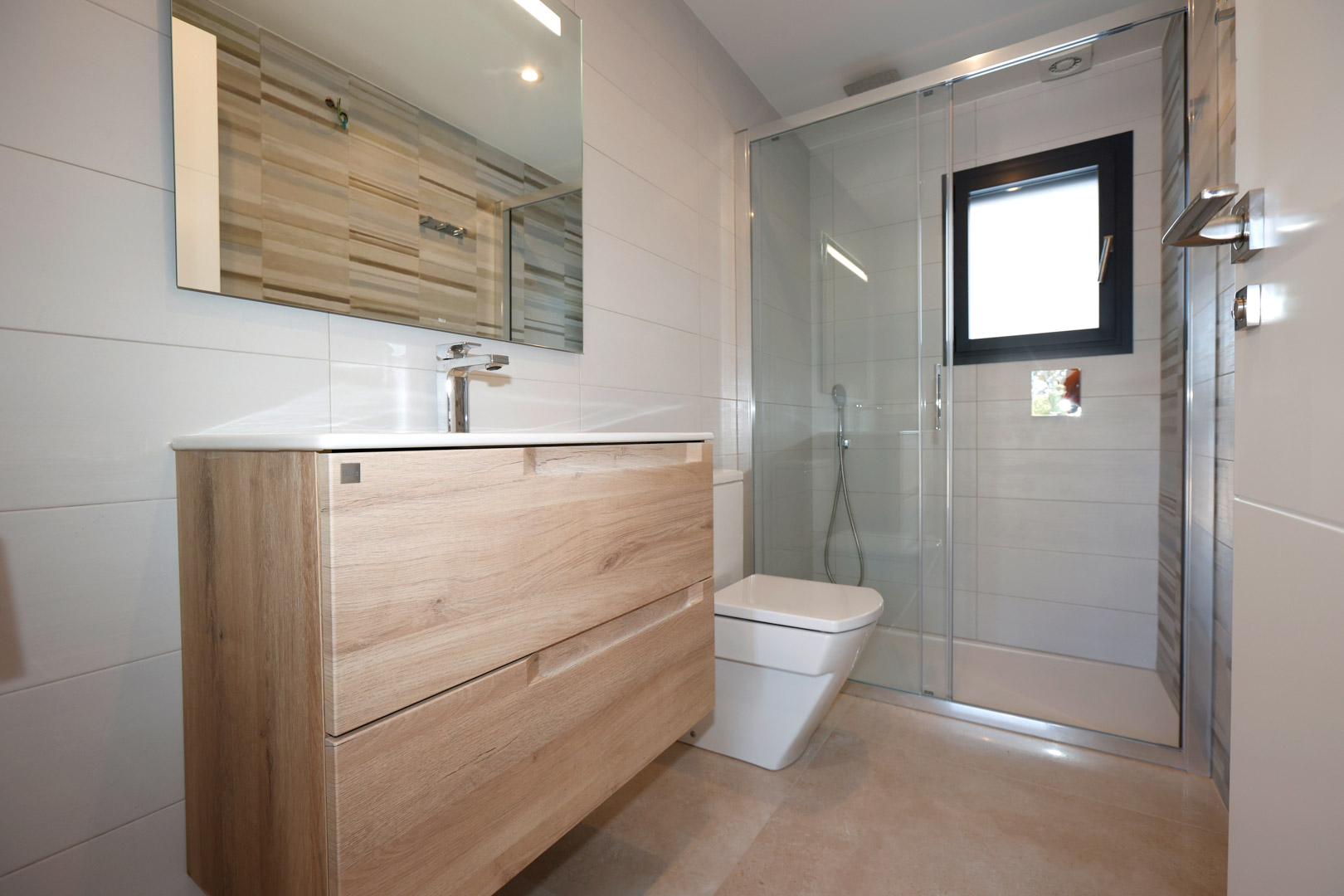 Baño contemporáneo con mueble de madera, lavabo integrado, ducha con mampara de cristal y acabados en gres porcelánico de tonos neutros.