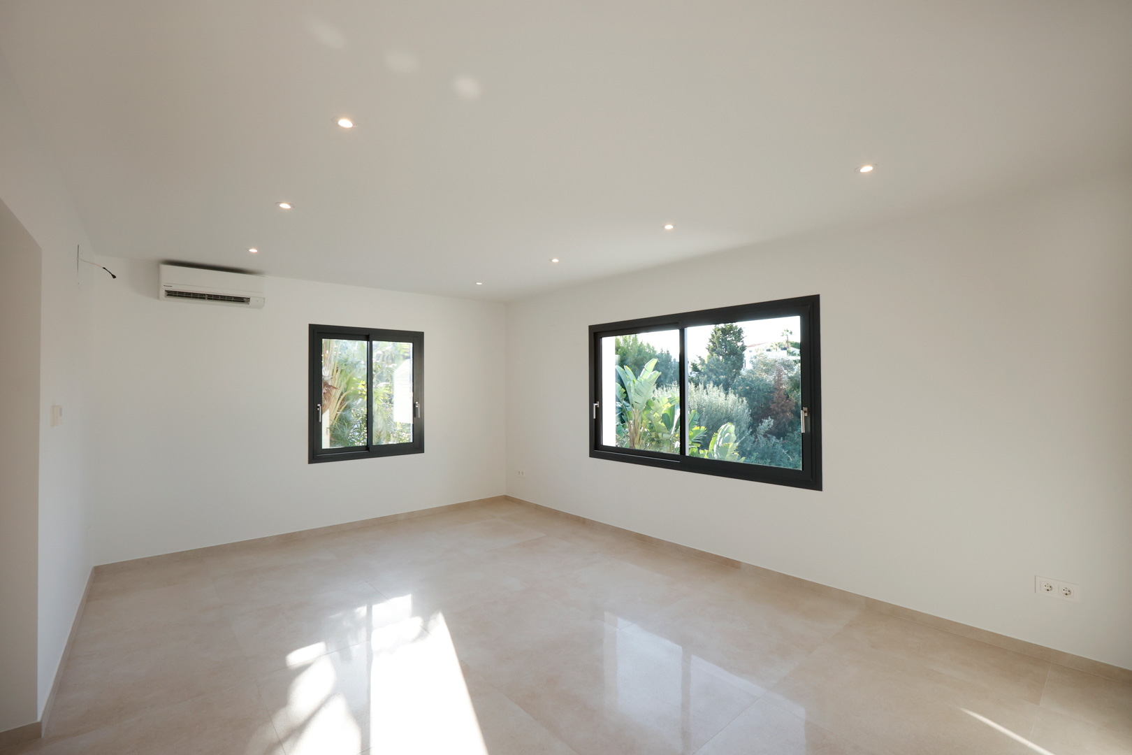 Habitación luminosa con suelo de gres porcelánico, iluminación LED empotrada, aire acondicionado y ventanas Technal con vistas al entorno natural.