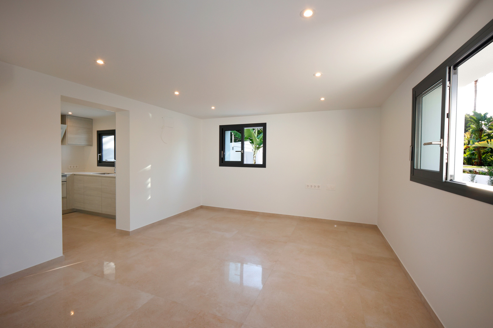 Salón-comedor diáfano con suelo de gres porcelánico, iluminación LED empotrada y ventanas Technal de doble acristalamiento con vistas al jardín.