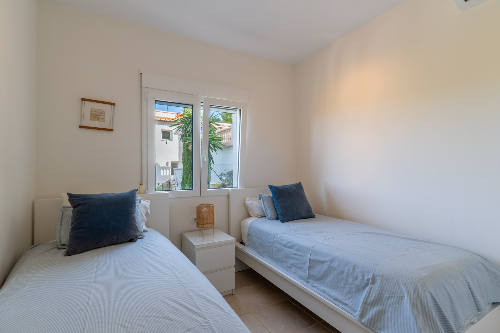 Dormitorio con dos camas individuales, paredes en tonos neutros y ventana de PVC que aporta luz natural. Incluye mesita de noche y suelos de gres.