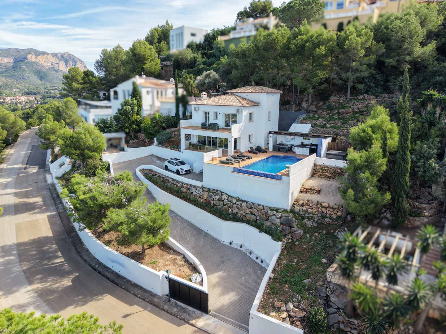 Vista aérea de la villa mediterránea con piscina privada, terrazas en varios niveles y cocina de verano, integrada en una parcela elevada con muros de piedra natural.