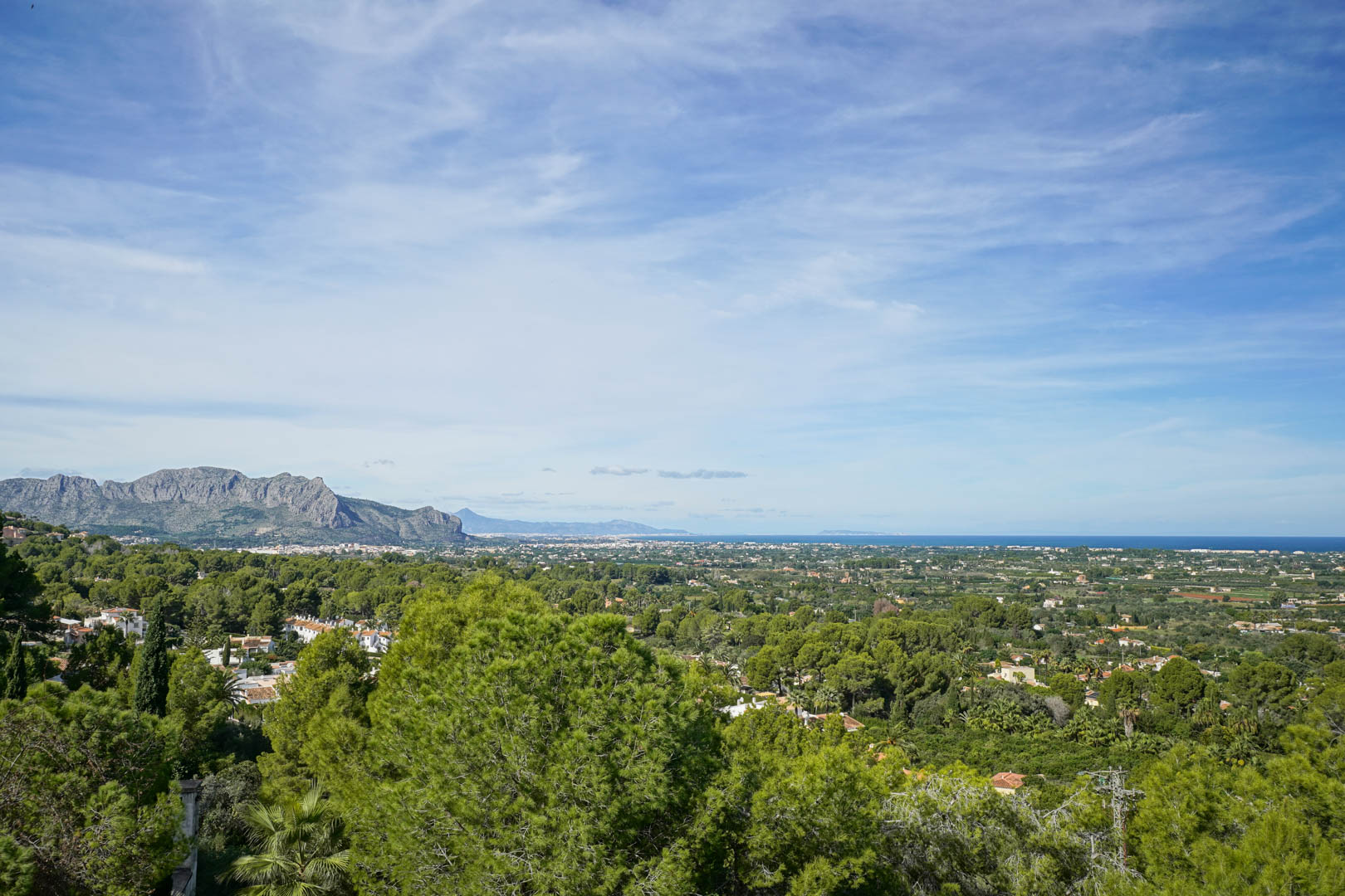 Vistas panorámicas desde La Sella que abarcan el macizo del Montgó, el valle costero y el mar Mediterráneo en el horizonte bajo un cielo despejado.