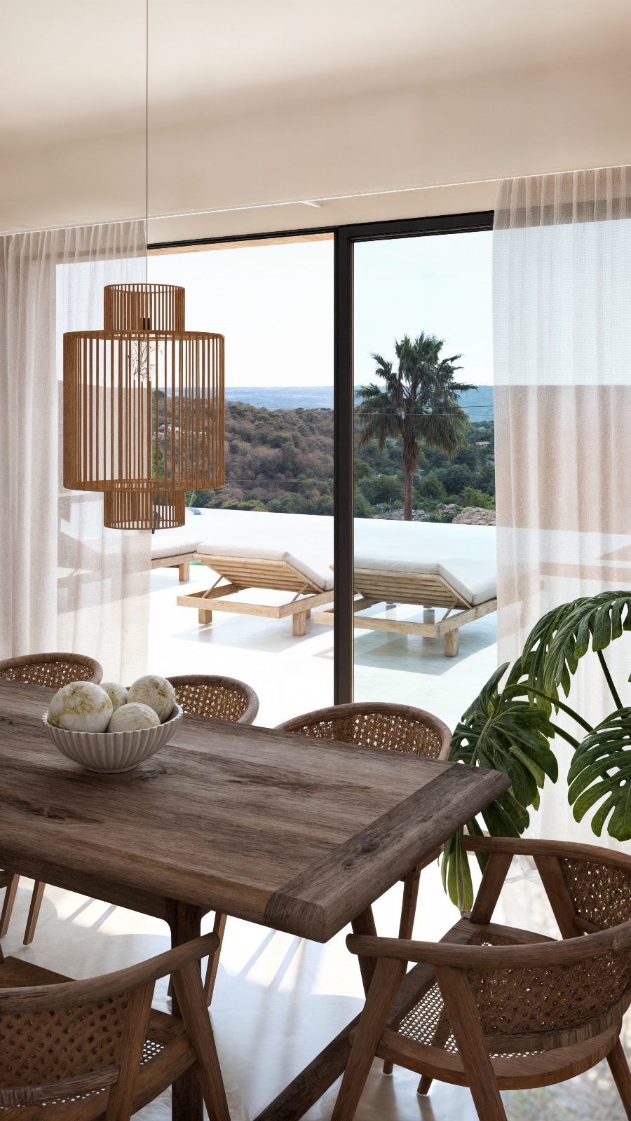 Comedor con mesa de madera maciza y lámpara de listones, con vistas a la terraza, piscina infinita y el paisaje mediterráneo a través de grandes ventanales.