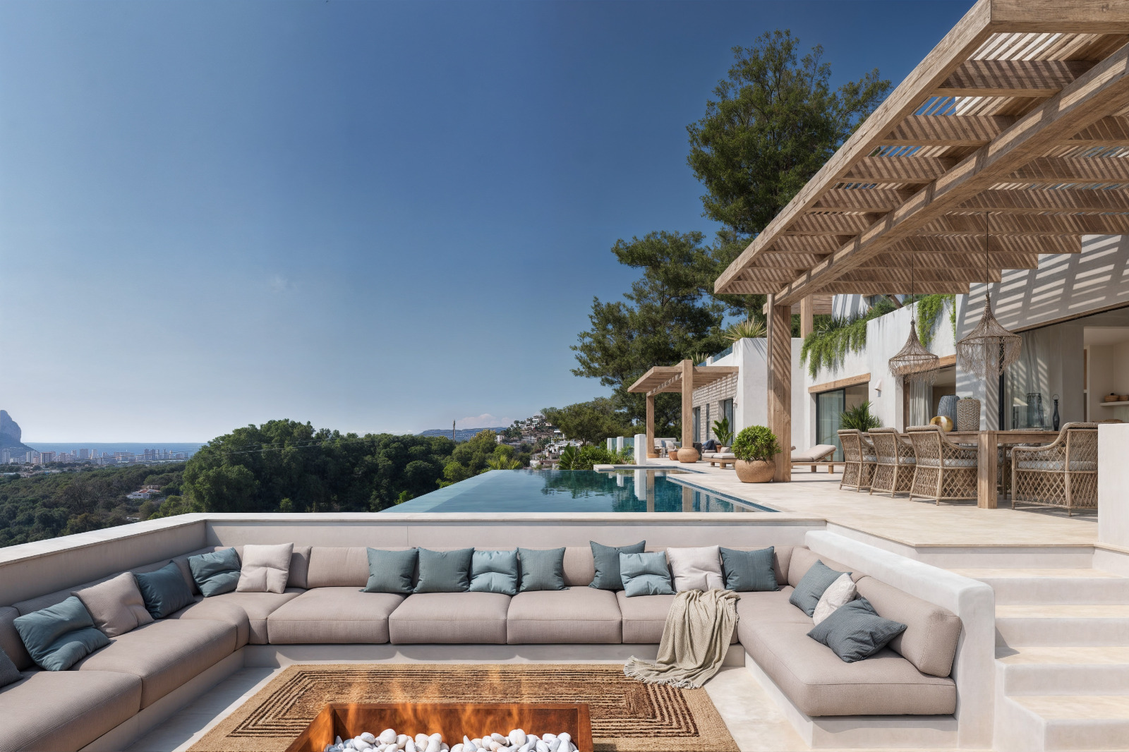 Zona de estar exterior hundida con brasero central, terraza con pérgola de madera y comedor, junto a una piscina infinita con vistas al mar y al Peñón de Ifach.