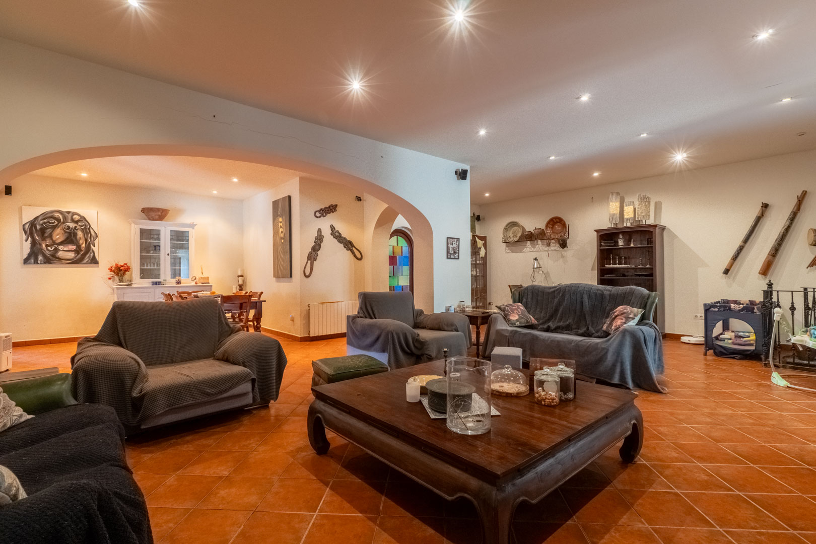 Amplio salón con suelo de terracota, iluminación empotrada y un gran arco arquitectónico que conecta con la zona de comedor y el resto de la planta baja.
