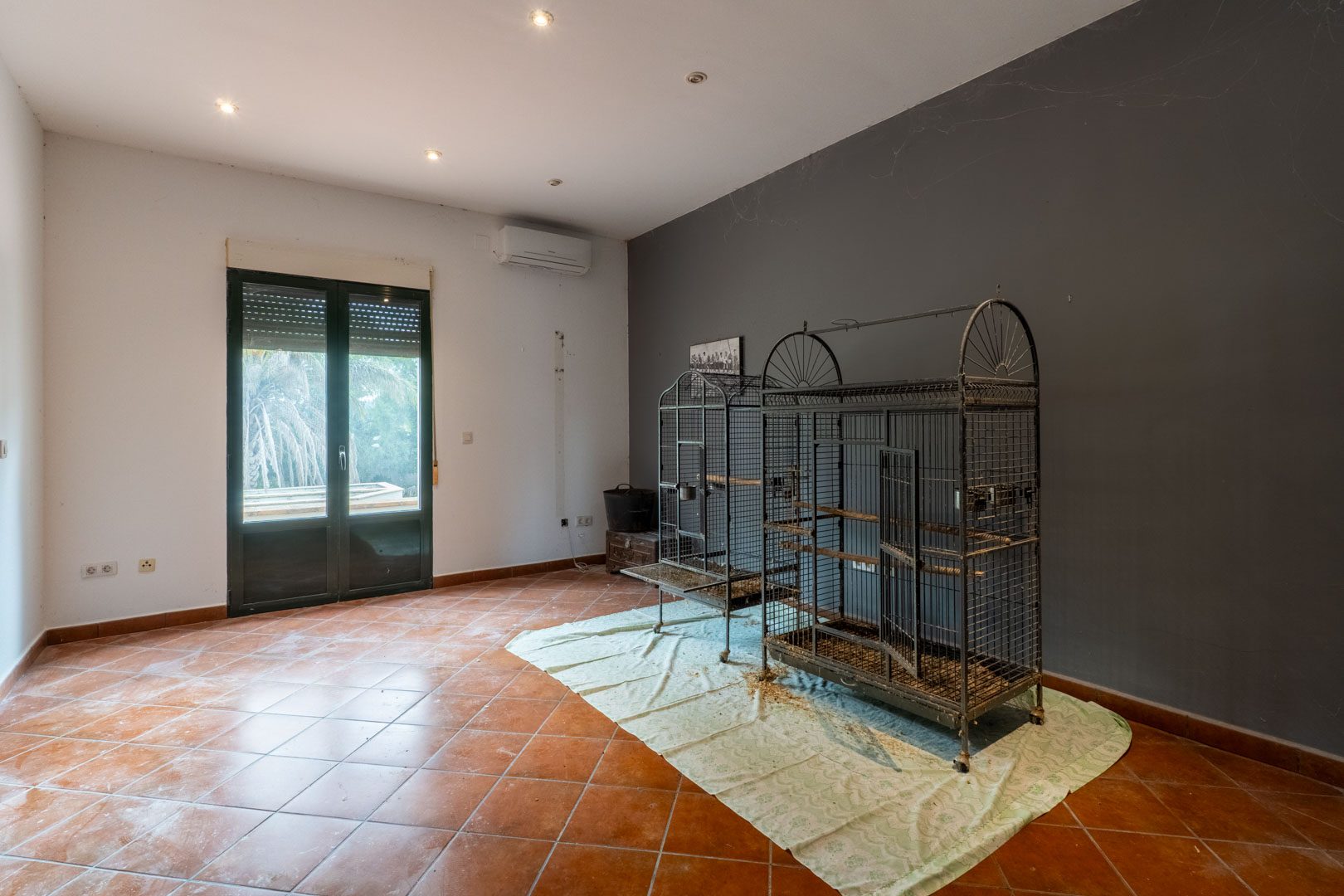 Habitación con suelo de baldosa de terracota, pared de acento gris y acceso directo al exterior. Incluye iluminación empotrada, aire acondicionado y vistas al jardín.