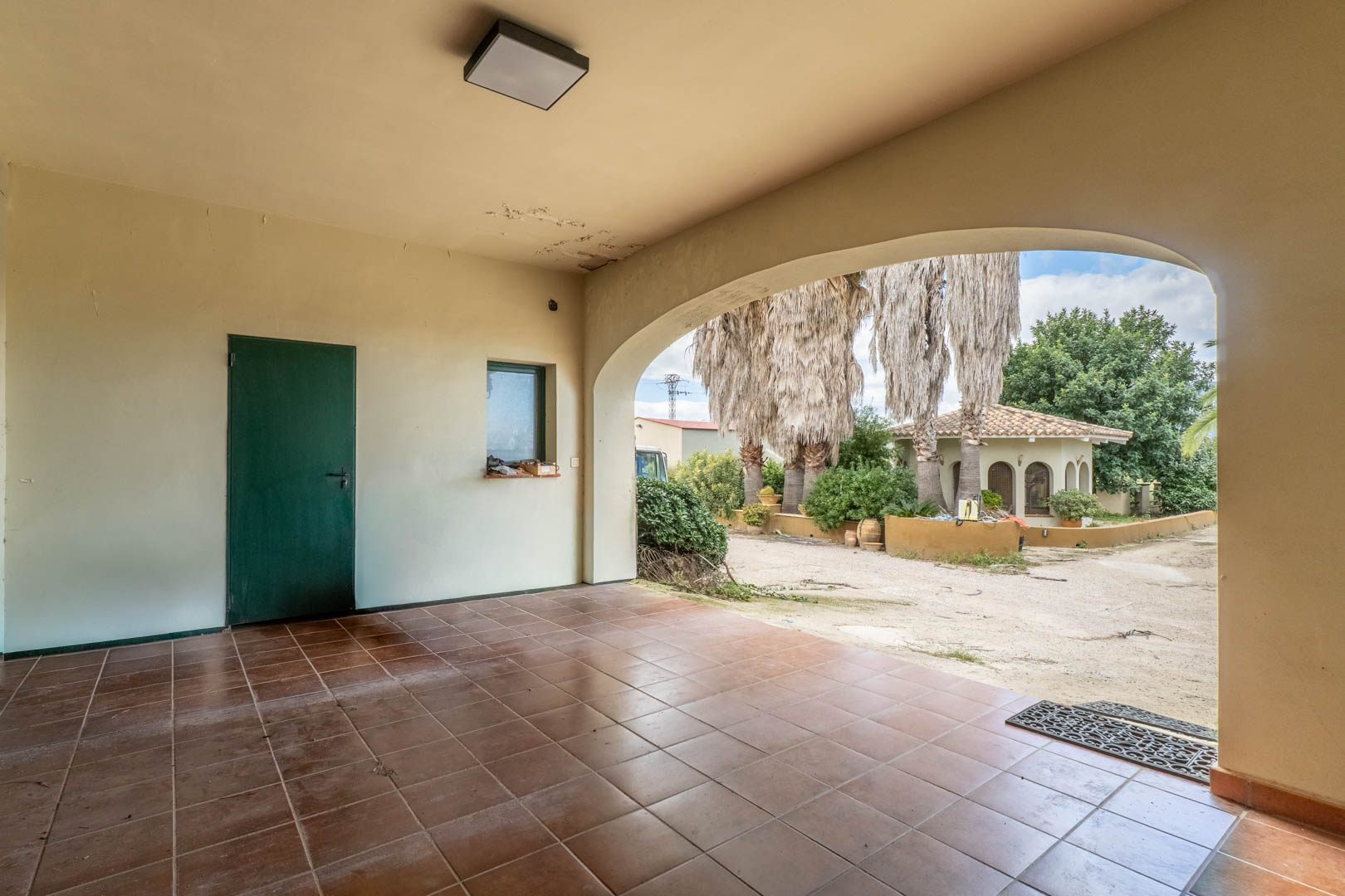 Porche cubierto con suelos de gres cerámico y arco de medio punto que ofrece vistas a los jardines mediterráneos y a la vivienda de invitados independiente.
