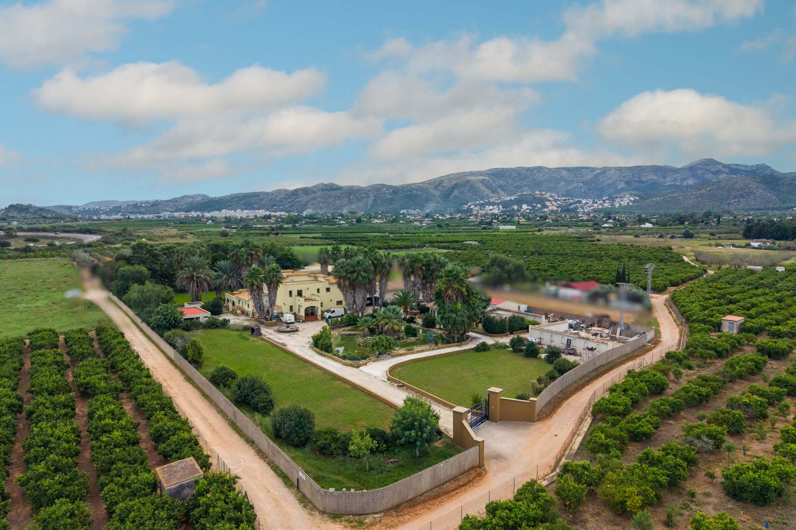 Vista aérea de la propiedad de 10.000 m² que muestra la casa principal, el estanque central y los jardines rodeados de extensos campos de cítricos y montañas.