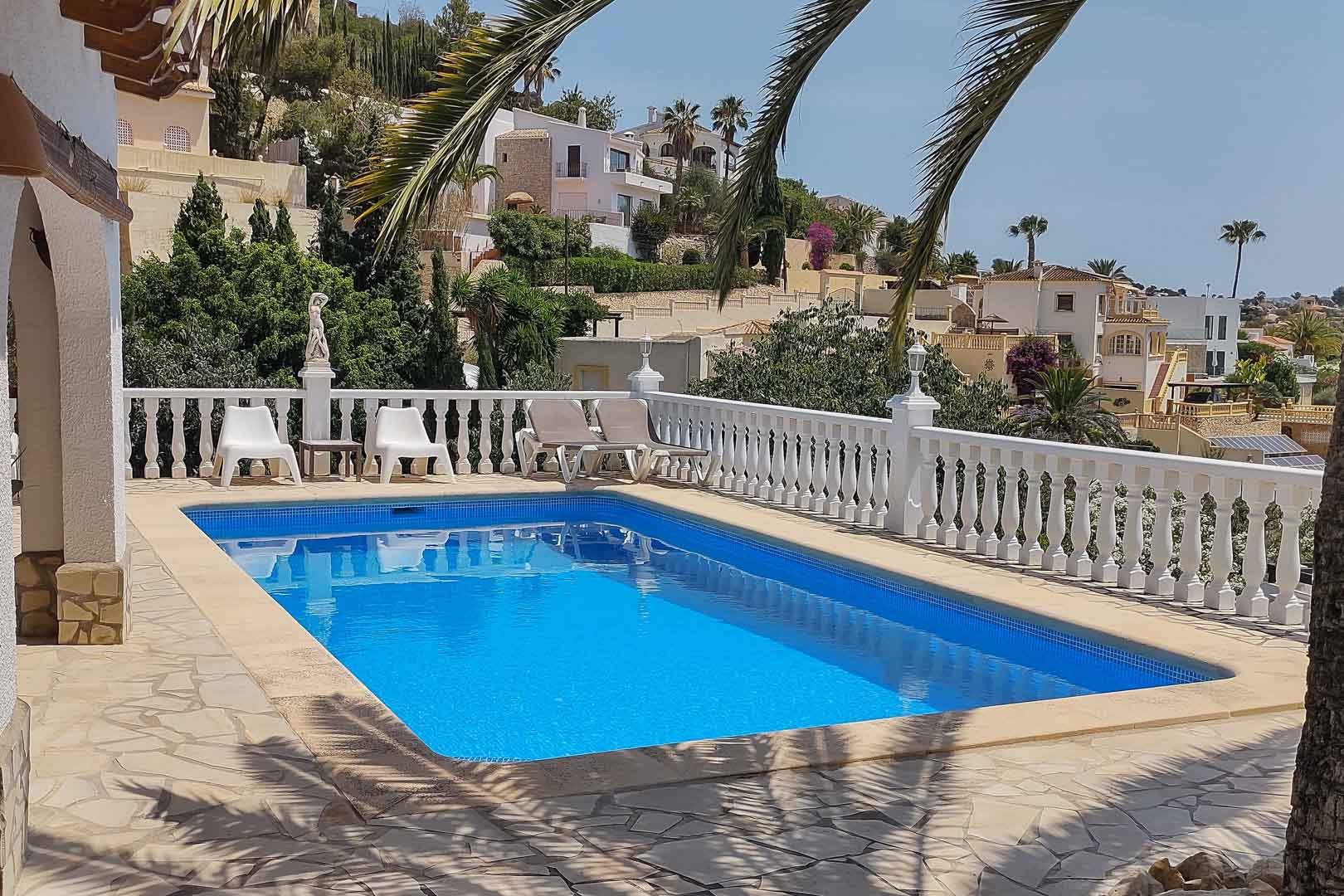 Piscina rectangular revestida en gresite azul, rodeada por una terraza de piedra irregular y una balaustrada blanca con vistas al valle y palmeras.