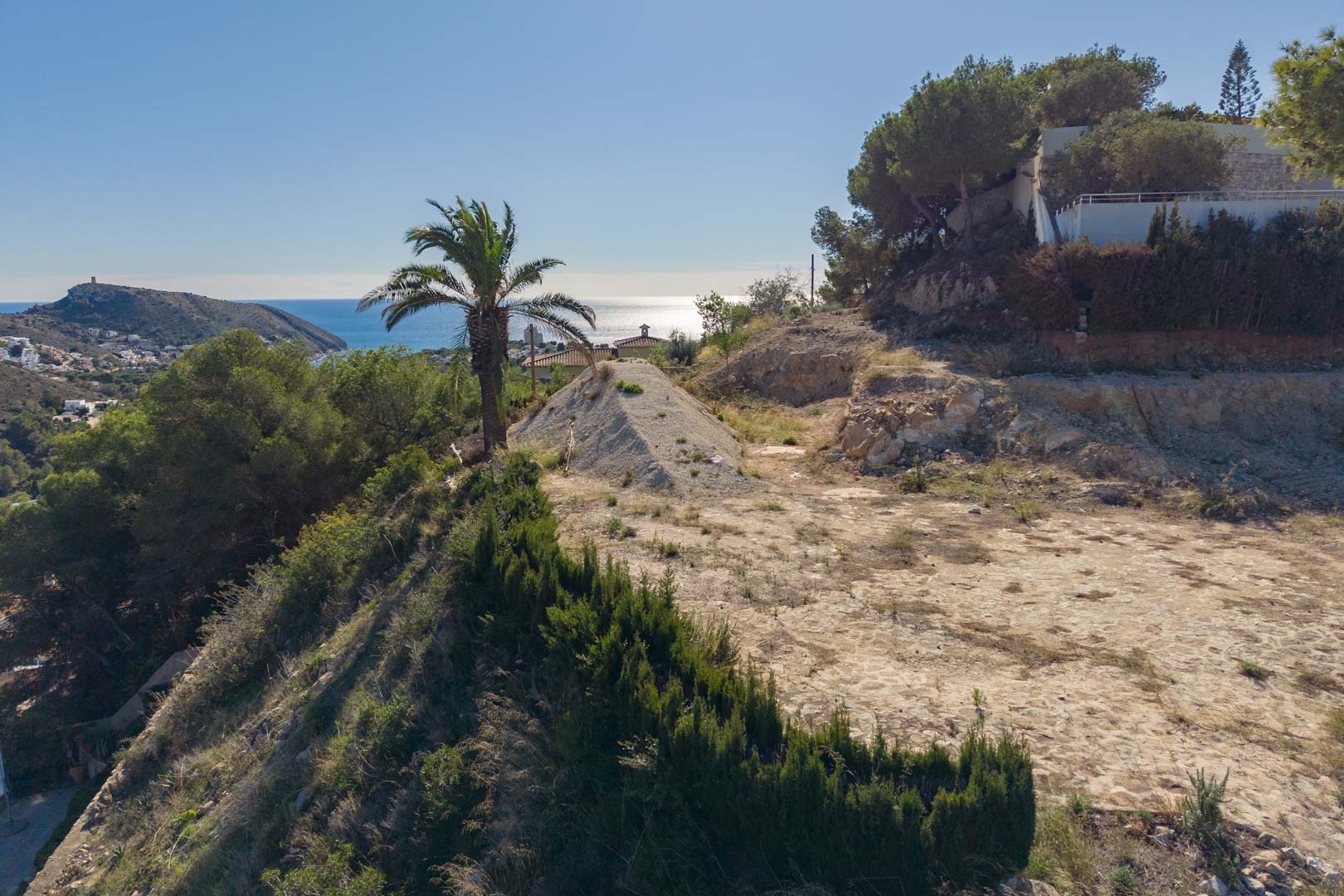 Parcela elevada en Moraira con vistas panorámicas al mar Mediterráneo y El Portet, rodeada de pinos y vegetación autóctona en un entorno natural privilegiado.