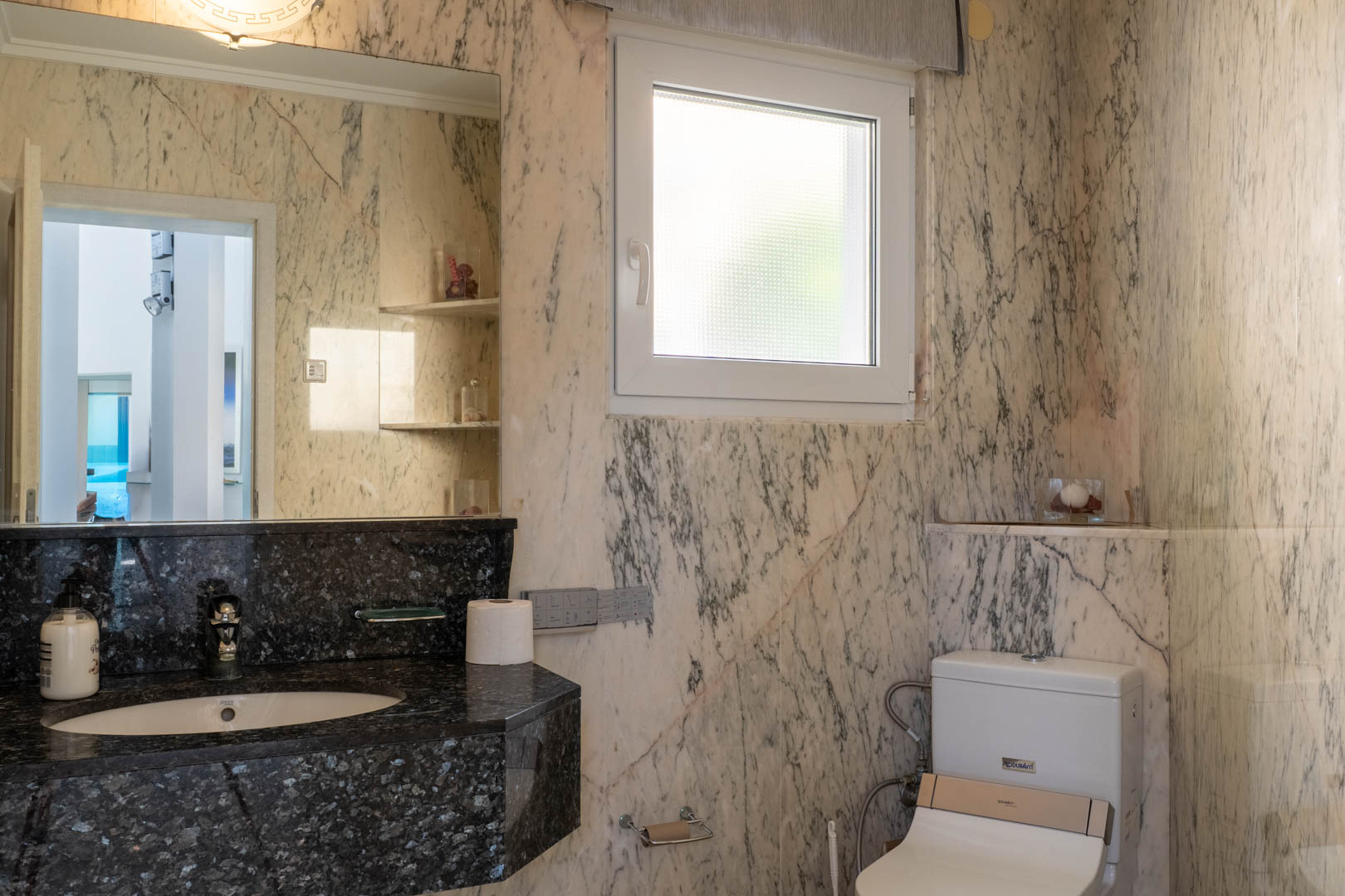 Cuarto de baño con paredes de mármol veteado y encimera de granito negro.