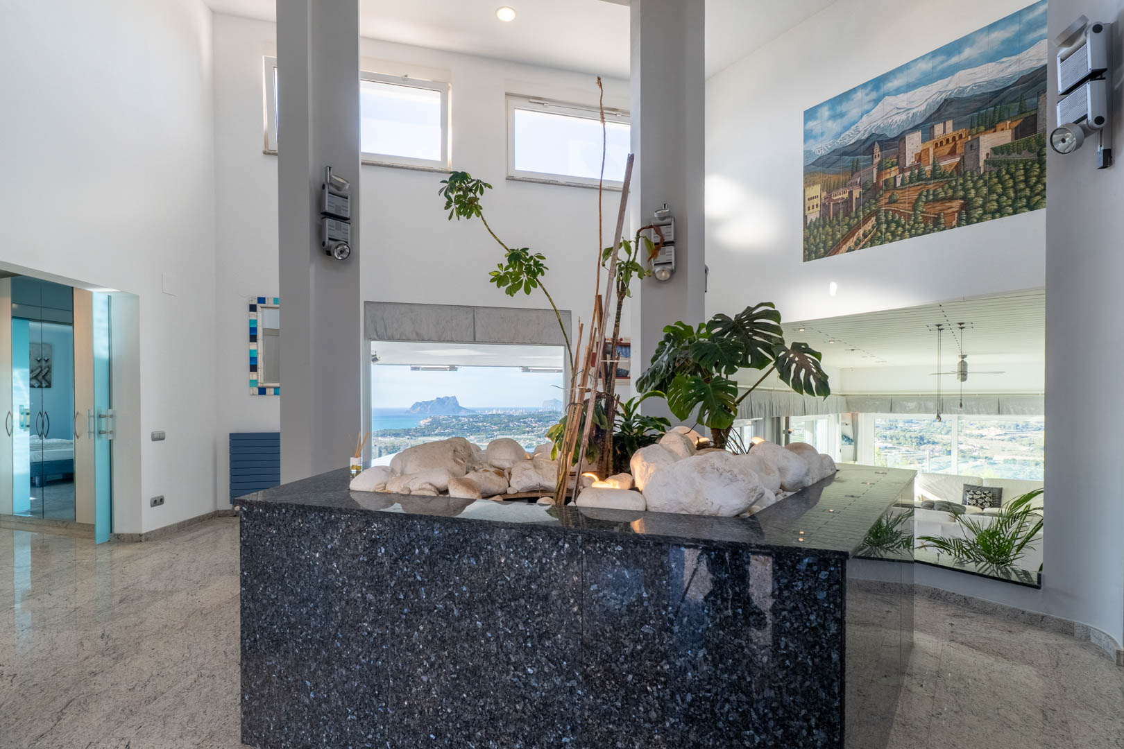 Detalle interior con encimera de granito pulido, plantas y vistas a la costa desde amplios ventanales.