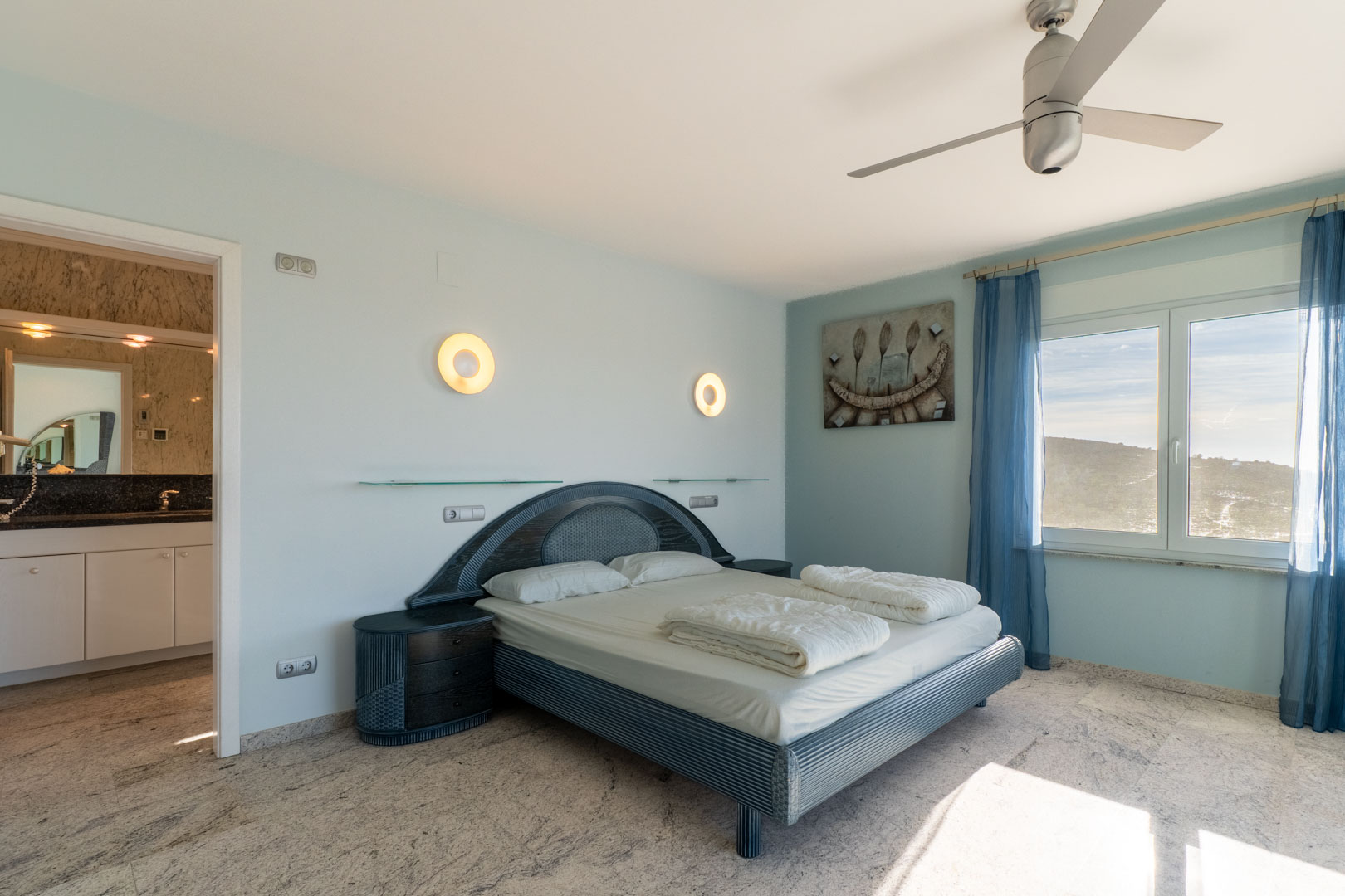 Dormitorio con cama doble de mimbre y baño en suite con encimera de granito.