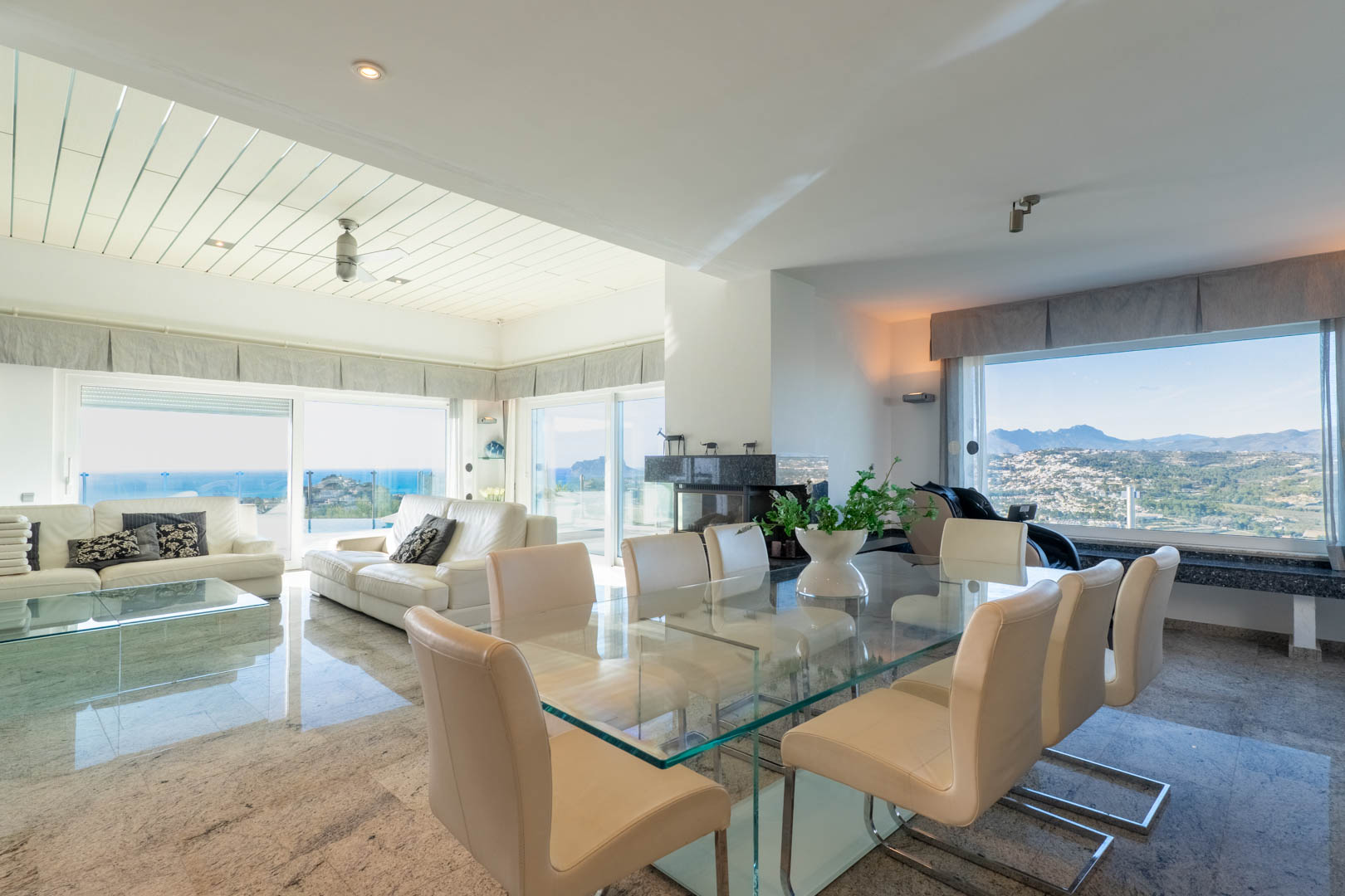 Luminoso comedor con mesa de cristal y vistas panorámicas al mar y la montaña.