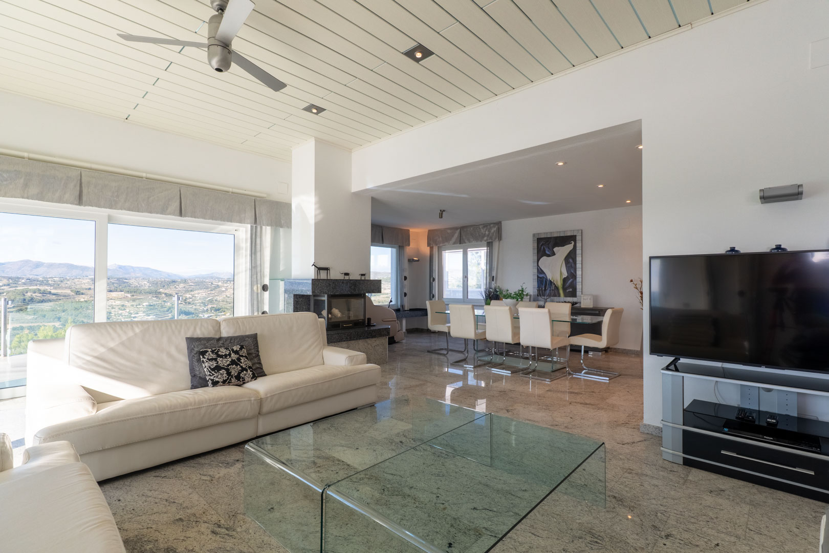Luminoso salón con suelos de mármol, sofá de cuero blanco y vistas panorámicas.