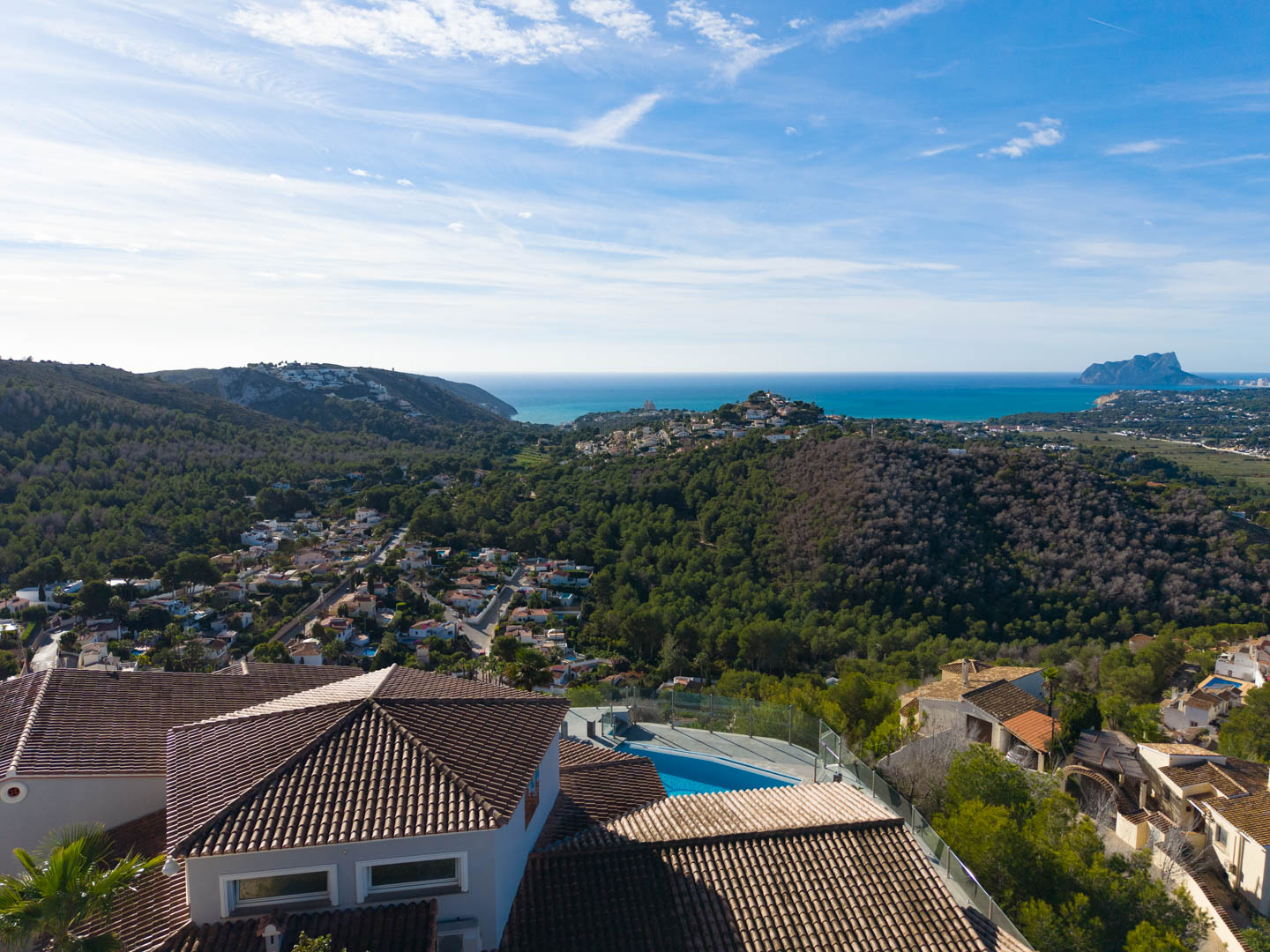 Vista aérea de la villa con tejas marrones, piscina azul y vistas panorámicas al mar y al paisaje verde.