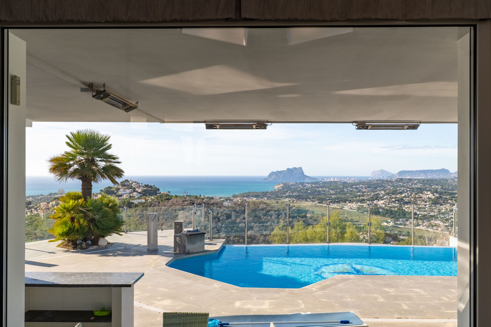 Vista desde el interior a la piscina privada con vistas al mar y al paisaje de Moraira.