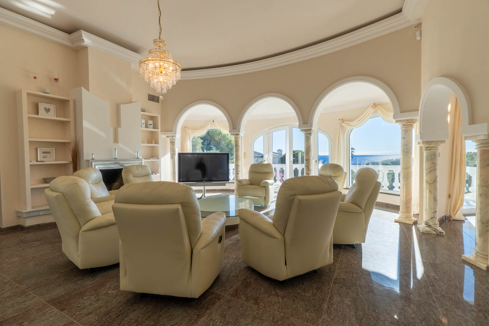 Salón circular con arcos sobre columnas de mármol, mobiliario de cuero crema y vistas panorámicas al Mediterráneo a través de amplios ventanales.