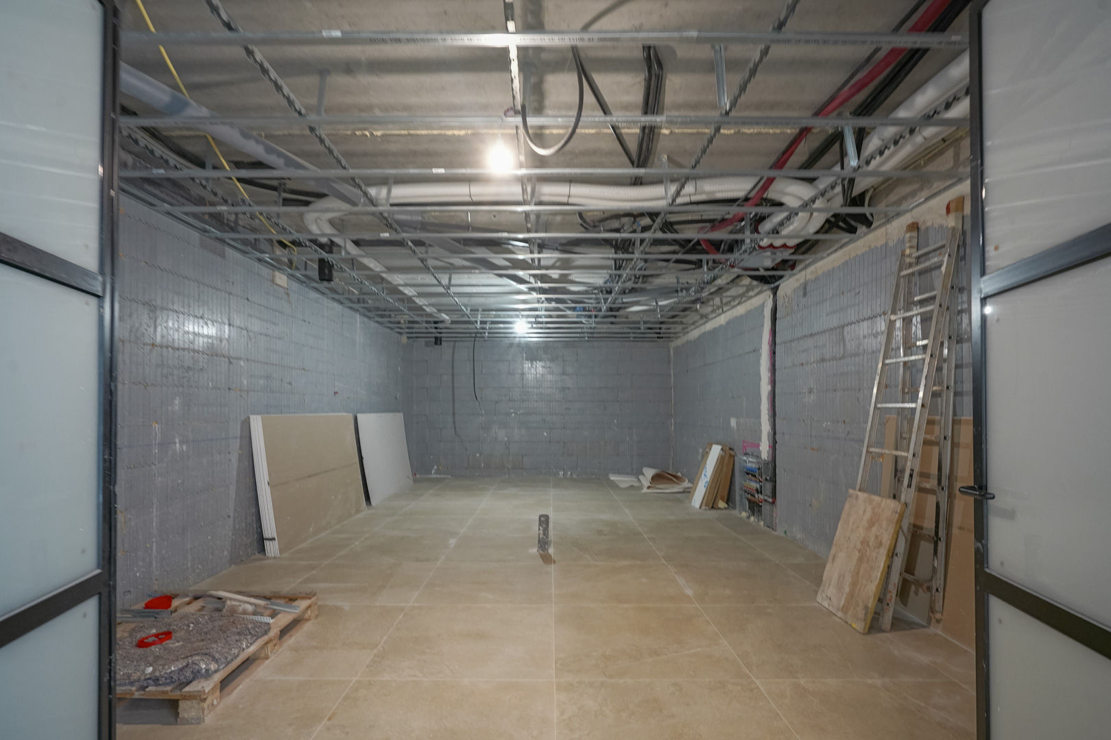 Sótano diáfano de 180 m2 en construcción con muros de Styro Stone, techos técnicos vistos y amplias puertas correderas de perfilería negra.