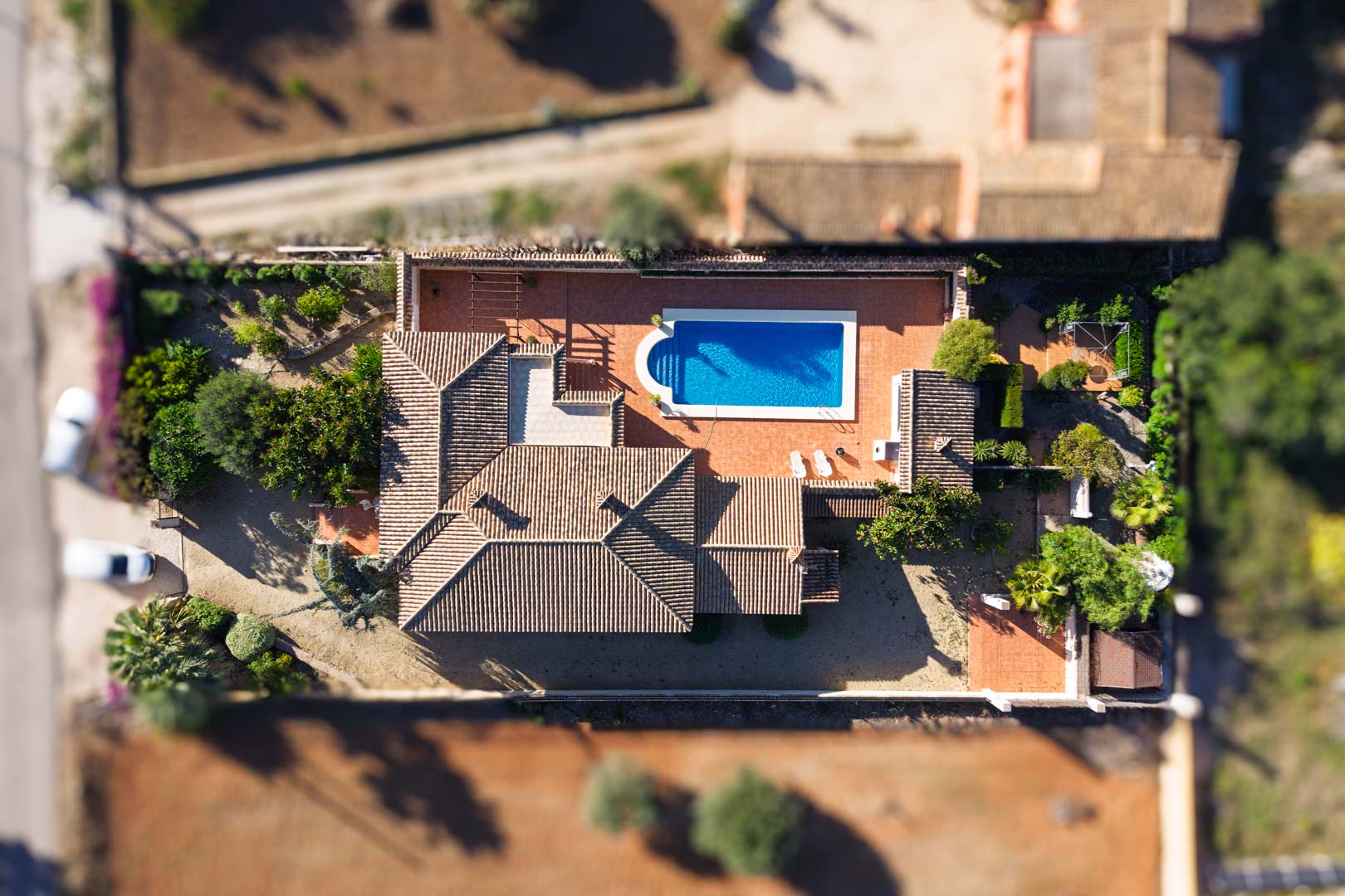 Vista aérea cenital de la villa sobre parcela llana, destacando la piscina rectangular, las amplias terrazas pavimentadas y la cubierta de teja cerámica tradicional.
