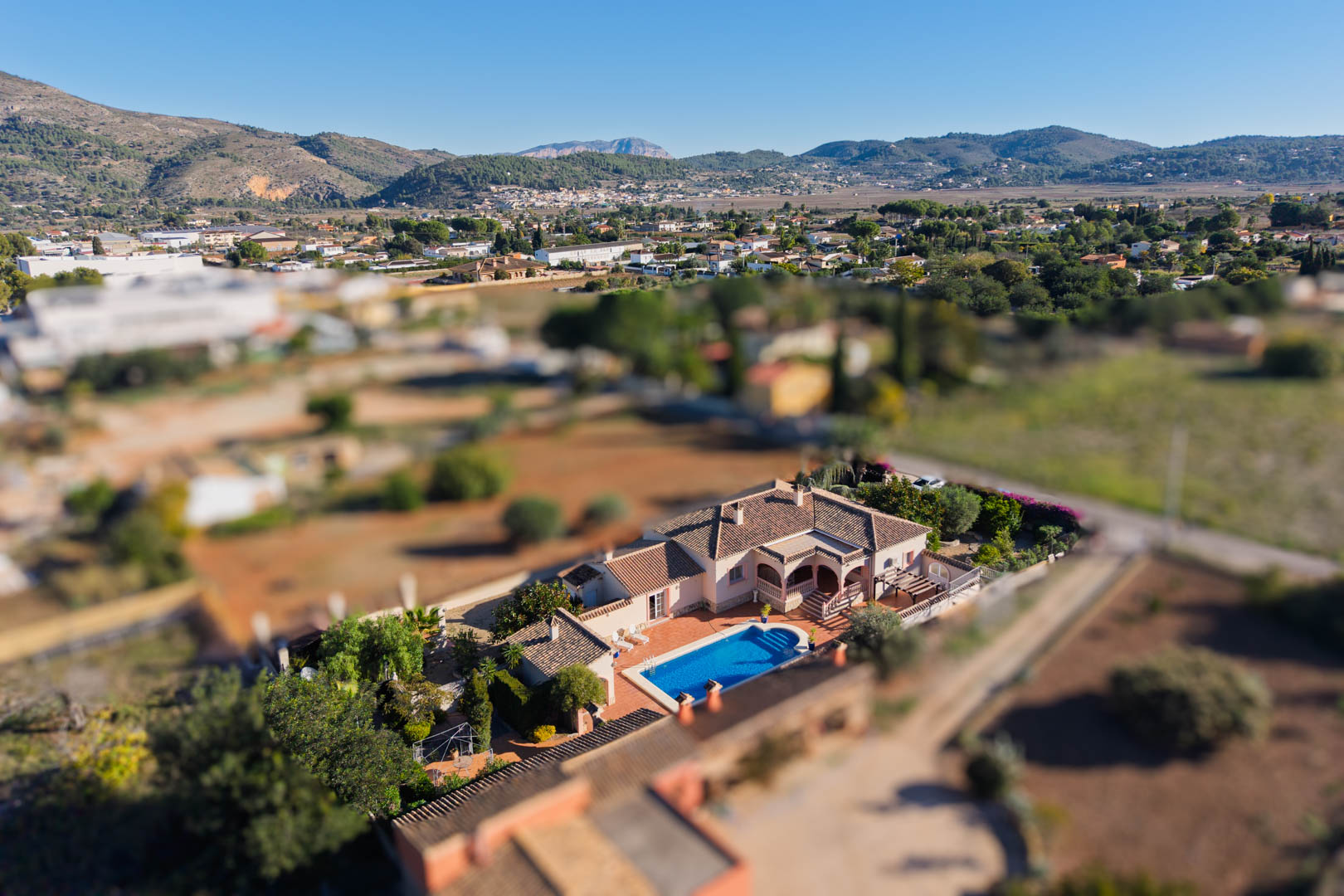 Vista aérea de la villa mediterránea en Jalón, destacando su piscina privada, amplia terraza y su ubicación en una parcela llana rodeada por el paisaje montañoso del valle.