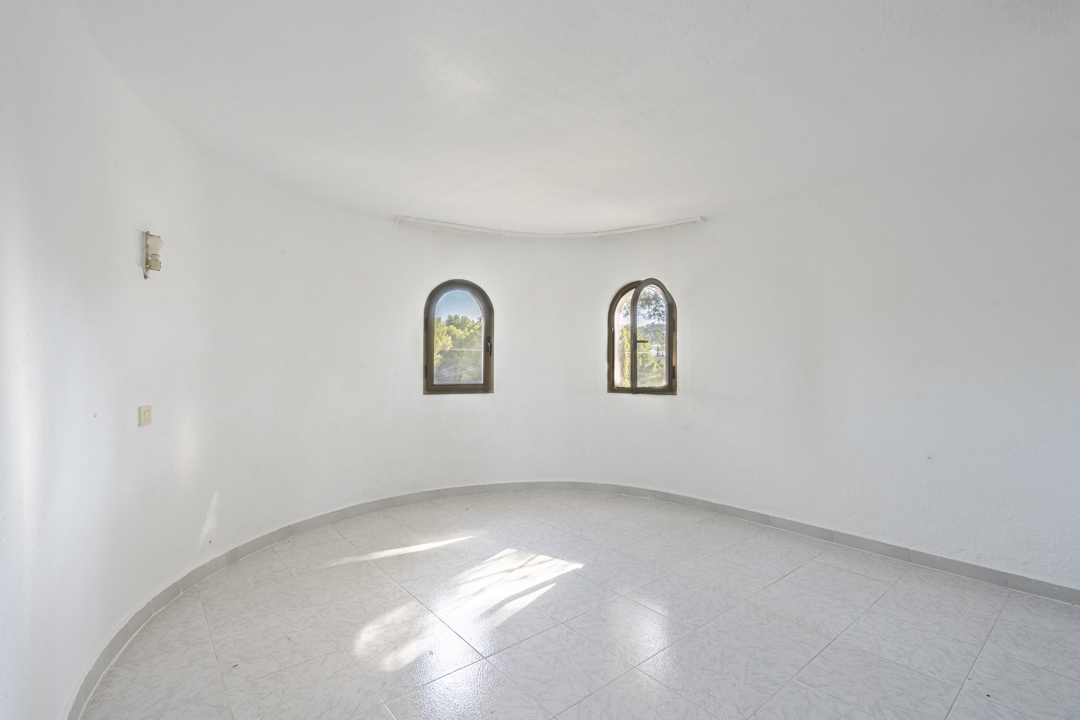 Habitación circular con paredes blancas, suelo de baldosas claras y dos ventanas de arco con vistas al entorno natural de Jávea.