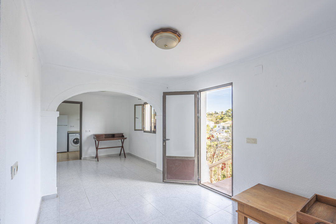 Salón luminoso con suelos cerámicos, un arco decorativo y acceso directo a la terraza exterior. Se aprecia la conexión con la cocina funcional.