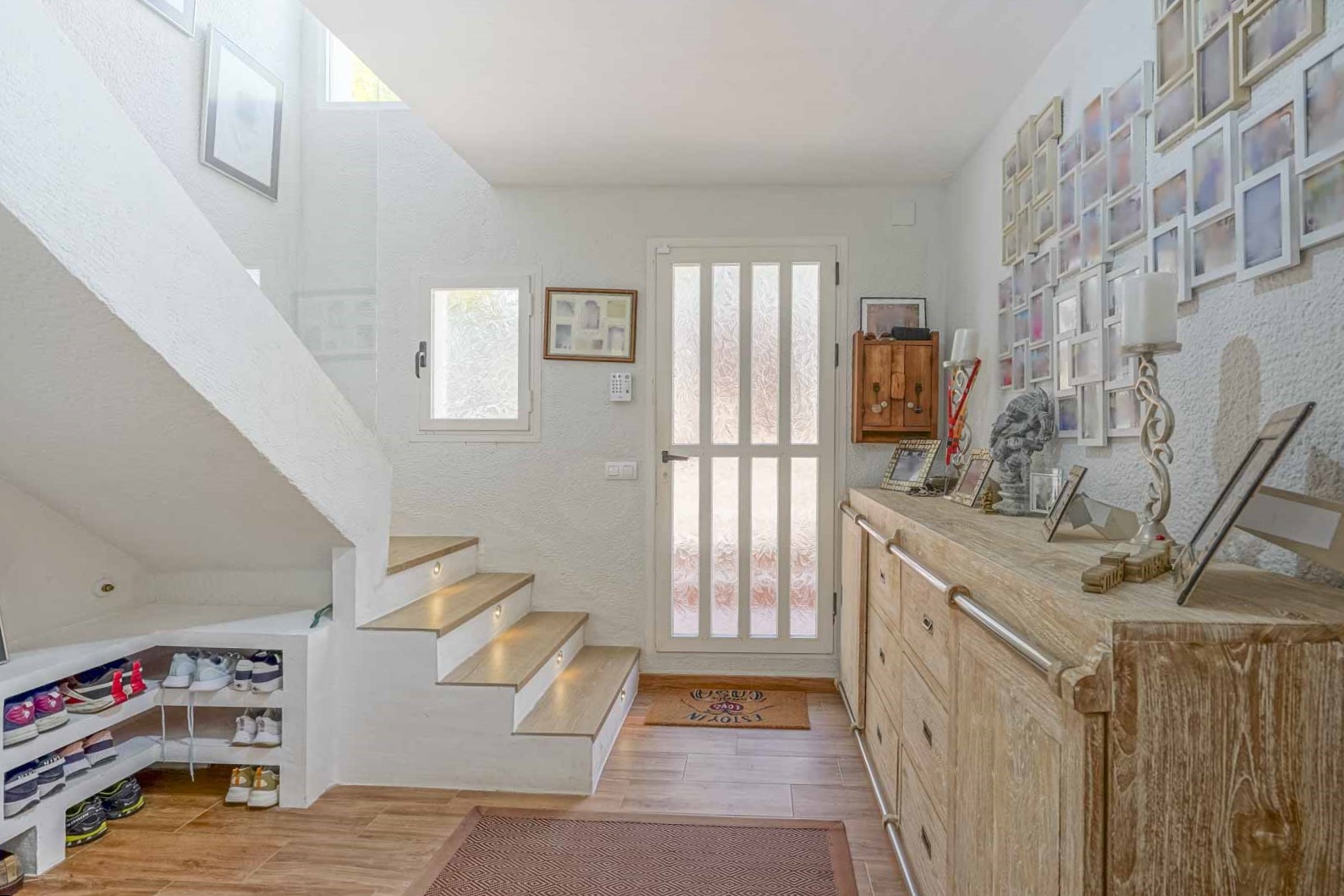 Vestíbulo luminoso con escalera de madera y luces LED integradas, aparador de madera rústica y práctico almacenamiento bajo el hueco de la escalera.