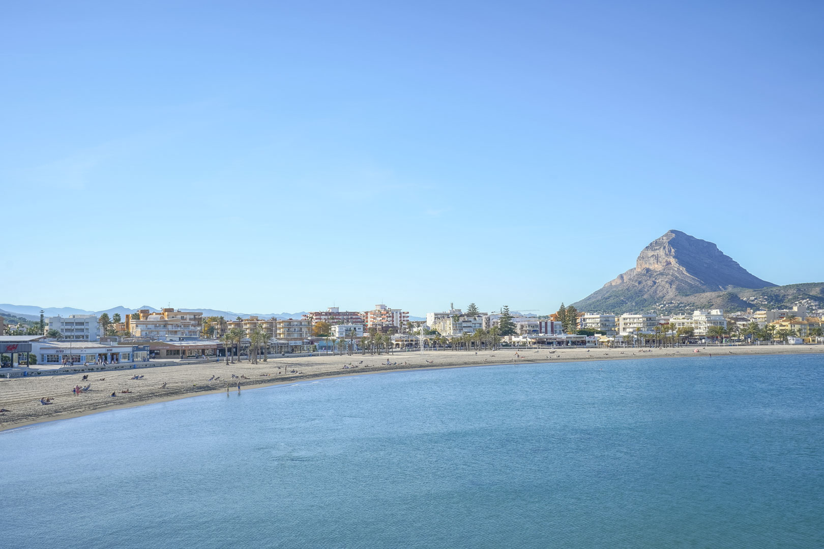 Vista panorámica de la playa del Arenal en Jávea, mostrando la bahía de aguas tranquilas y el emblemático monte Montgó al fondo.