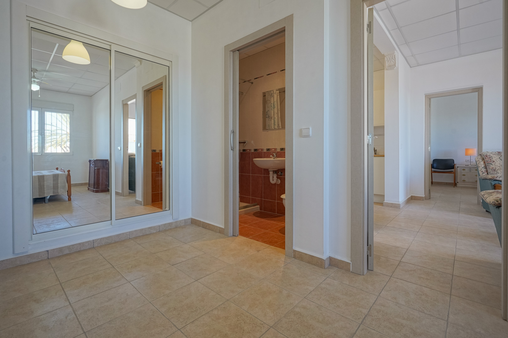 Pasillo distribuidor con suelos cerámicos, armario empotrado de puertas correderas espejadas y acceso directo a un baño alicatado y estancias principales.